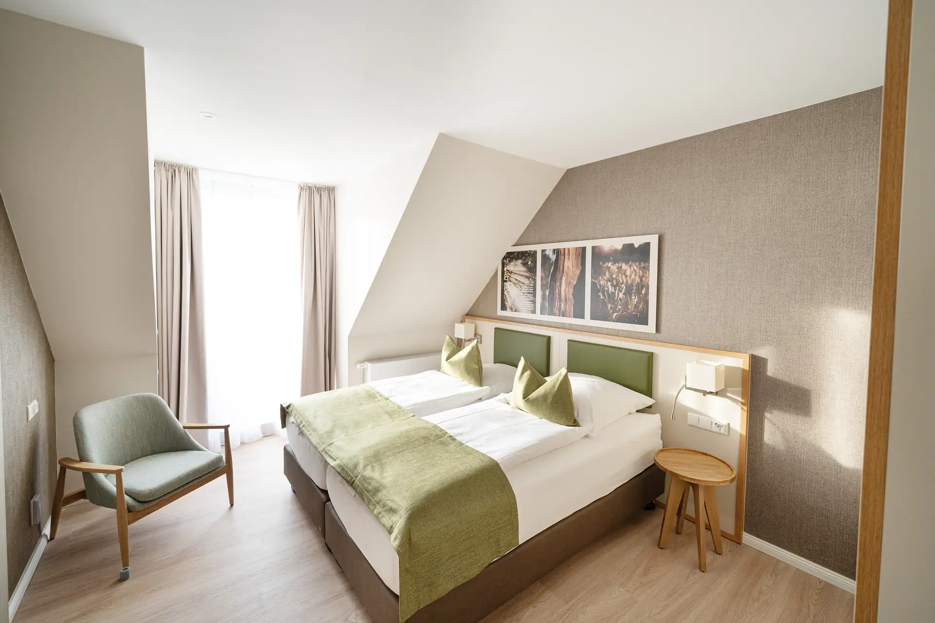 Beech Resort Plauer See: Hell eingerichtetes Schlafzimmer mit zwei Einzelbetten, grünen Bettläufern und Kissen, einem Sessel und zwei Bildern an der Wand.