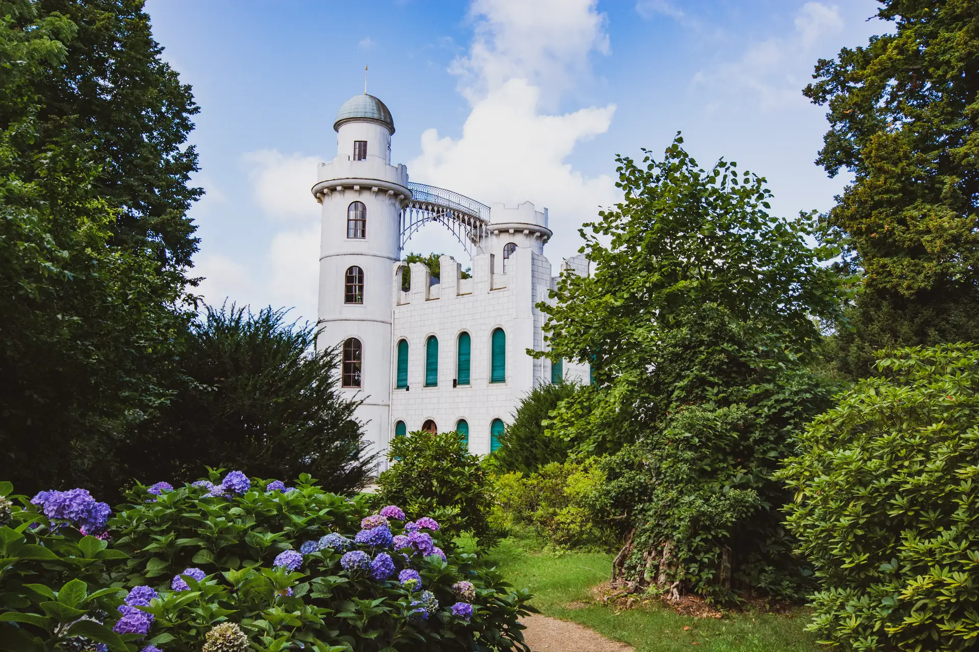 Schloss Pfaueninsel mit runden Türmen und Brücke, umgeben von grünen Bäumen und blühenden Hortensien in der Havel bei Berlin und Potsdam.