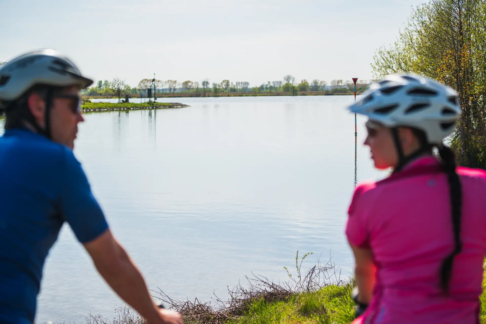 Zwei Radfahrer mit Helmen stehen an der Havel und blicken auf das ruhige Wasser und die Landschaft