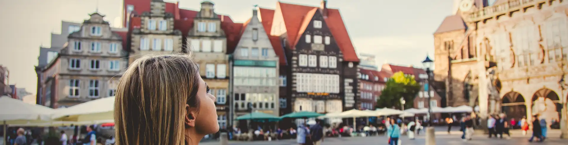 Person mit langen Haaren von hinten vor historischen Fachwerkhäusern auf einem belebten Platz in Bremen