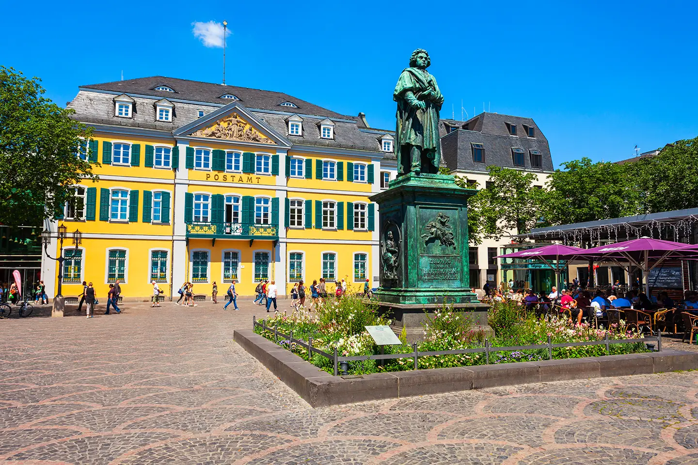 Beethovens Bronzestatue auf Münsterplatz vor altem Postamt dem ehemaligen Stadtpalais in gelb mit grünen Fensterläden in Bonn