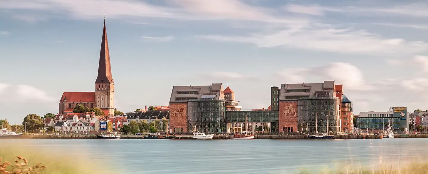 Blick von einem Holzsteg übers Wasser auf die Stadt Rostock