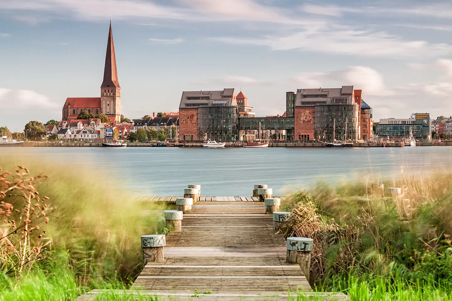 Blick von einem Holzsteg übers Wasser auf die Stadt Rostock