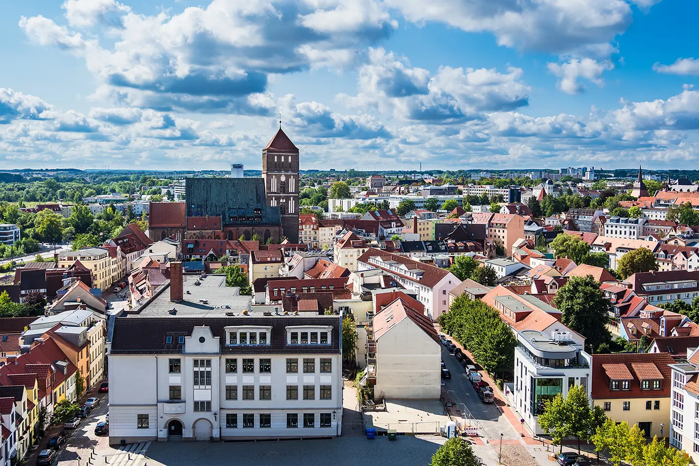 Blick von oben auf die Stadt Rostock mit blauem Himmel und weißen Wolken hinter der Nikolaikirche