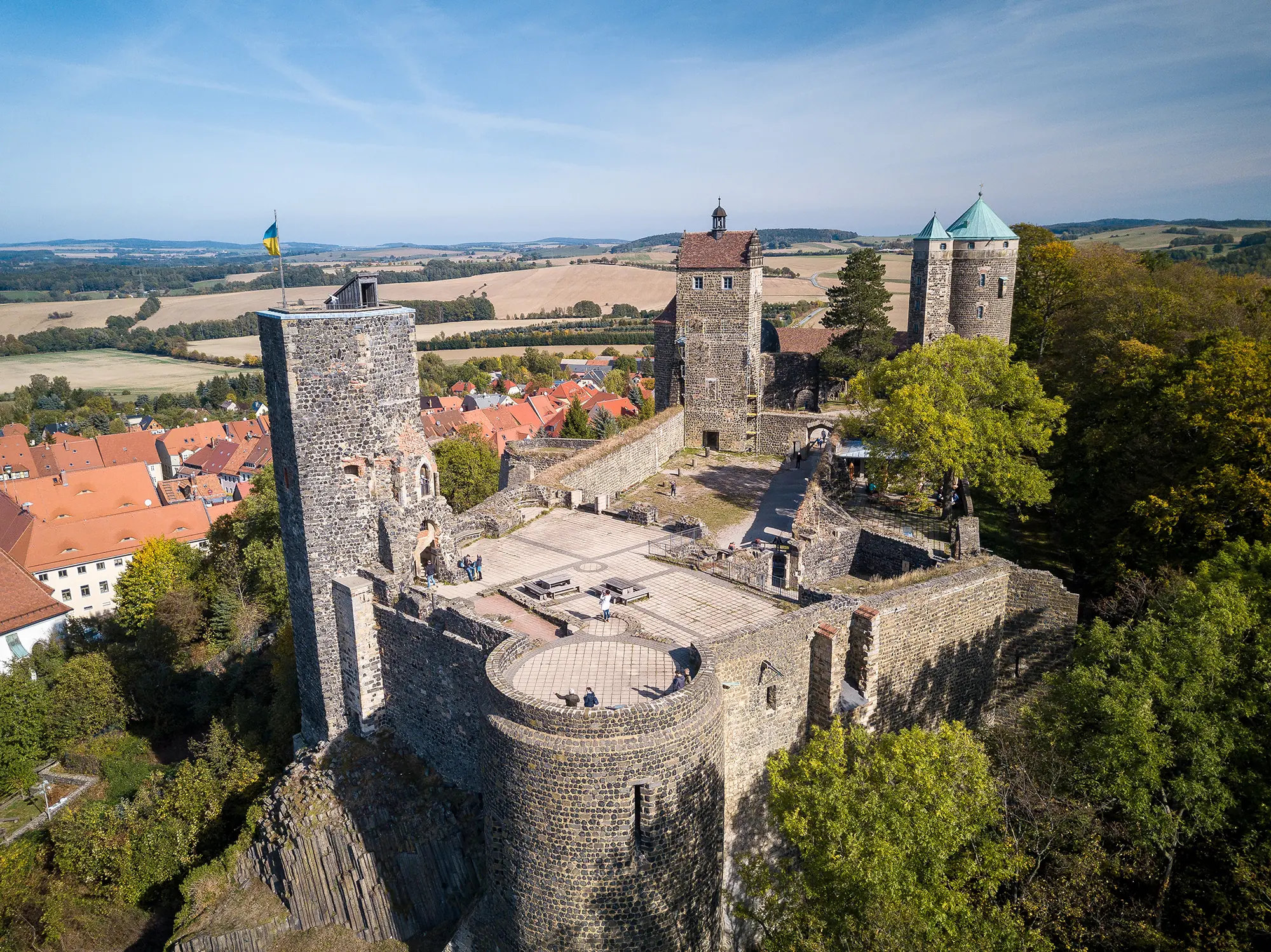 Panoramablick auf Burg Stolpen bei Dresden, vor grünem Wald, mit Feldern im Hintergrund und der Burg selbst im Bild.