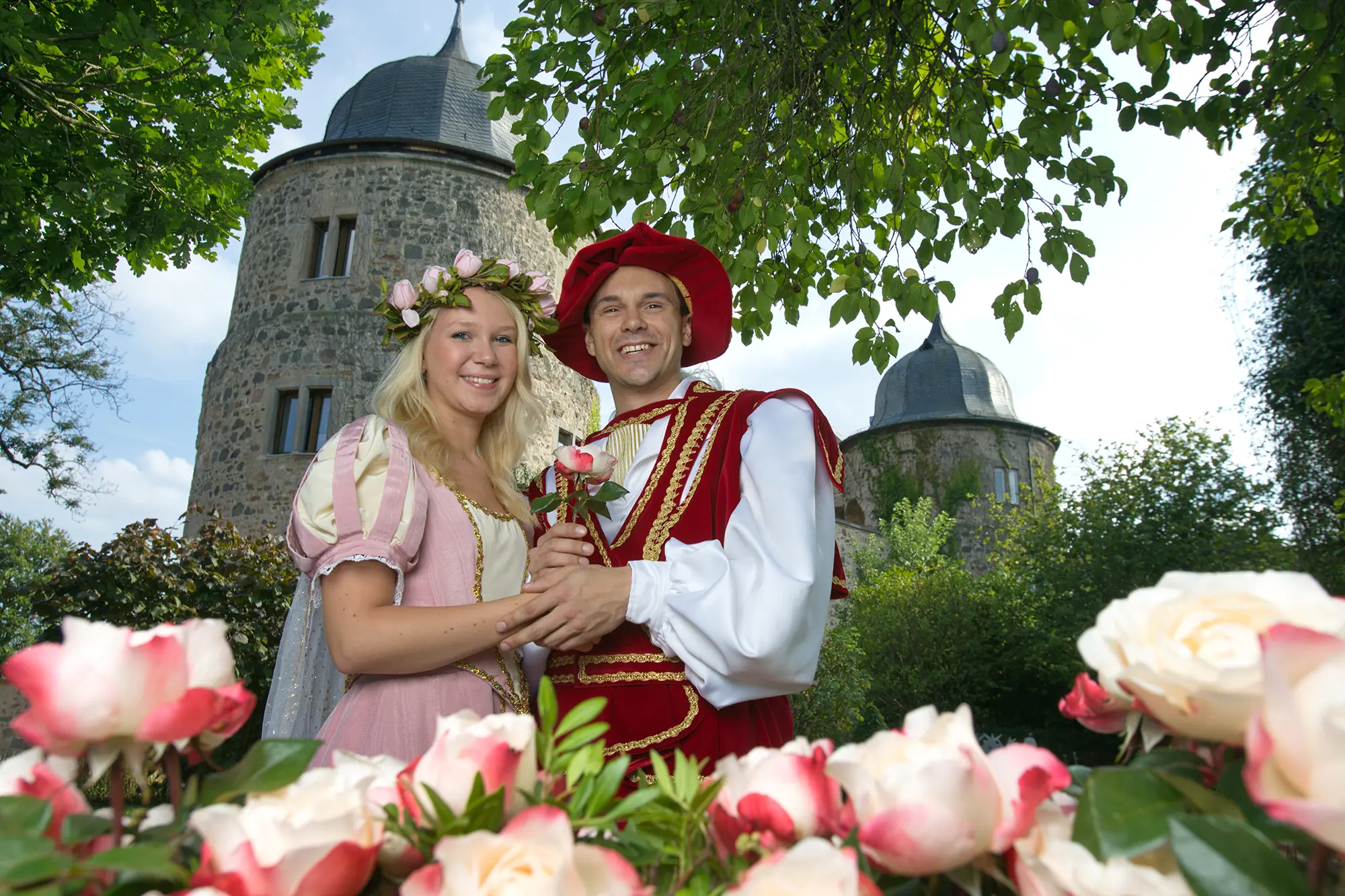 Schloss Sababurg, bekannt als Dornröschenschloss, mit Dornröschen und dem Prinzen, umgeben von Rosen im Vordergrund.