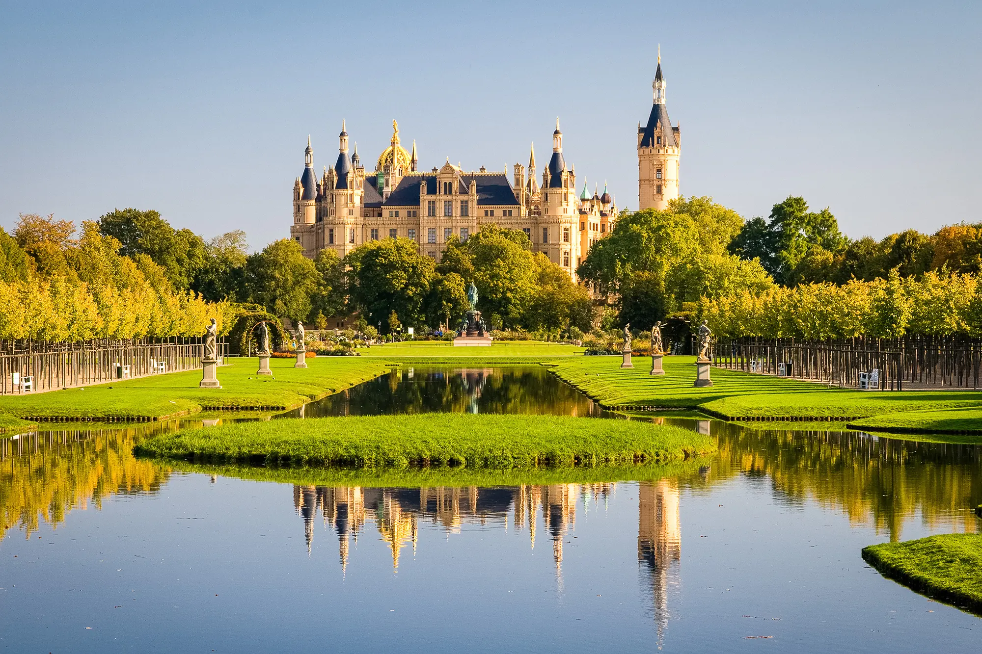 Schloss Schwerin bei Sonnenschein, gesehen aus dem Garten über einen Teich hinweg.