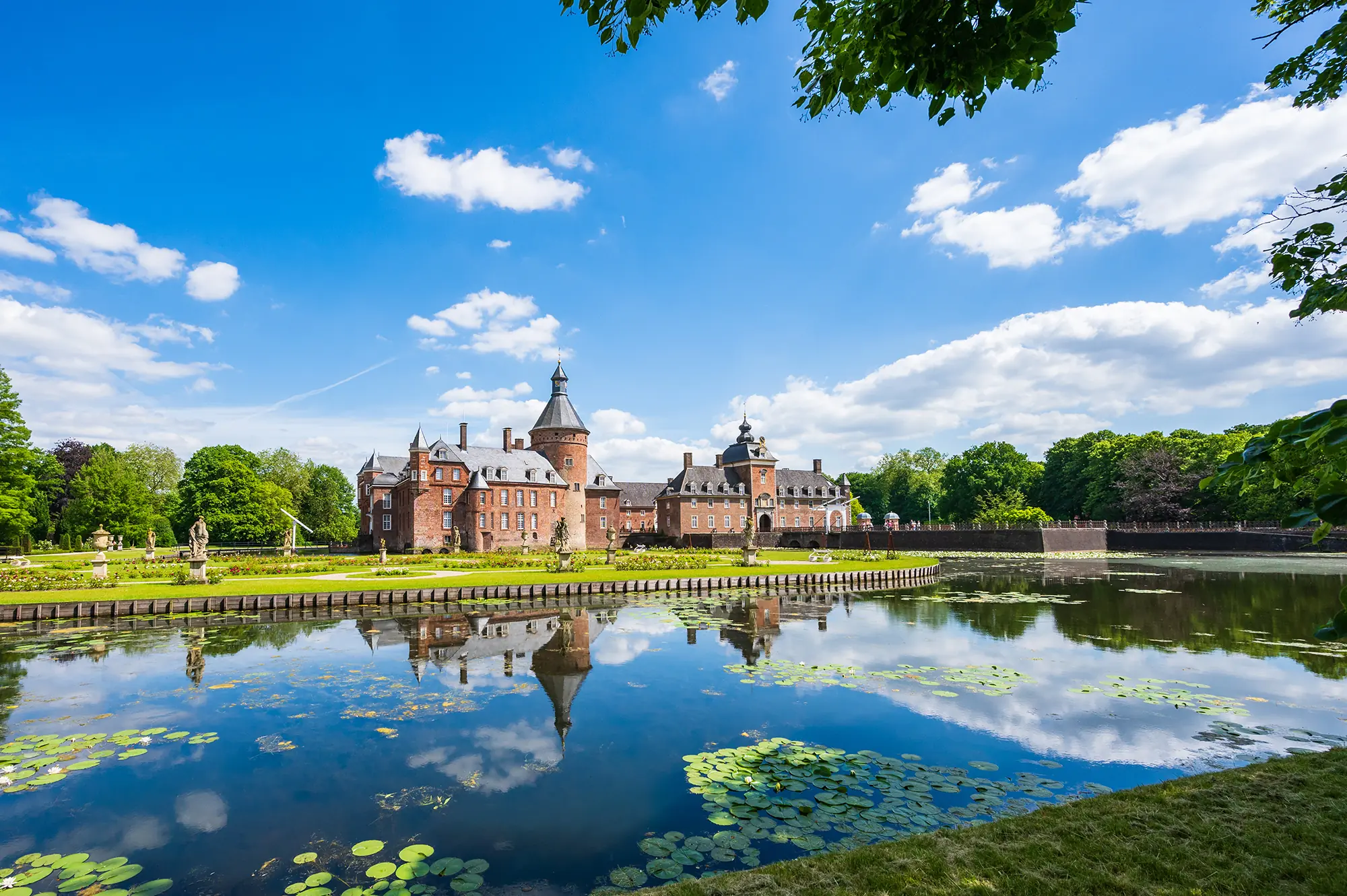 Wasserburg Anholt bei Bocholt, gesehen vom Garten aus über einen Teich mit Seerosen.