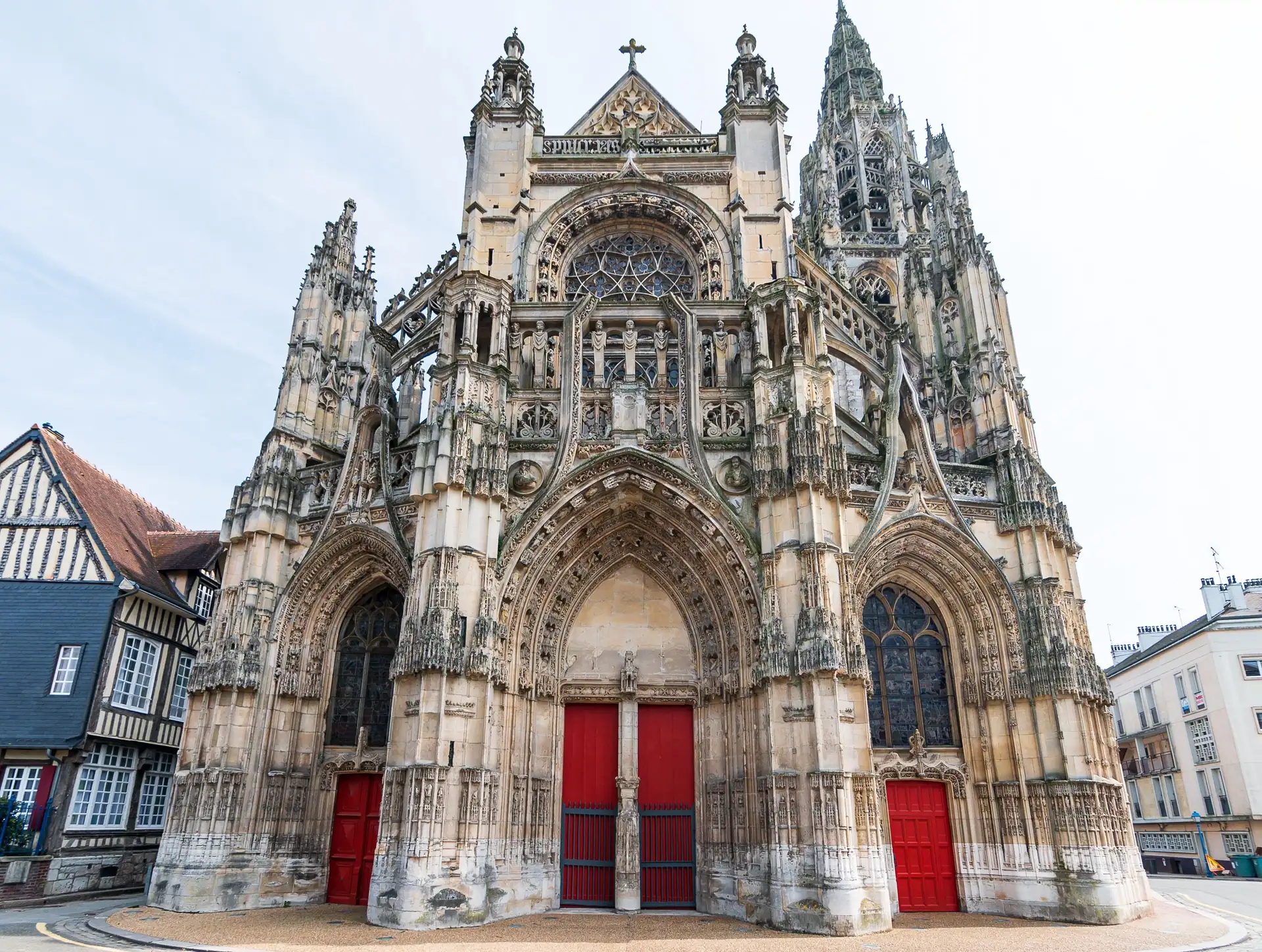Caudebec-en-Caux: Gotische Kathedrale mit drei roten Türen, reich verzierten Bögen und hohen Türmen, umgeben von Fachwerkhäusern und weiteren Gebäuden.