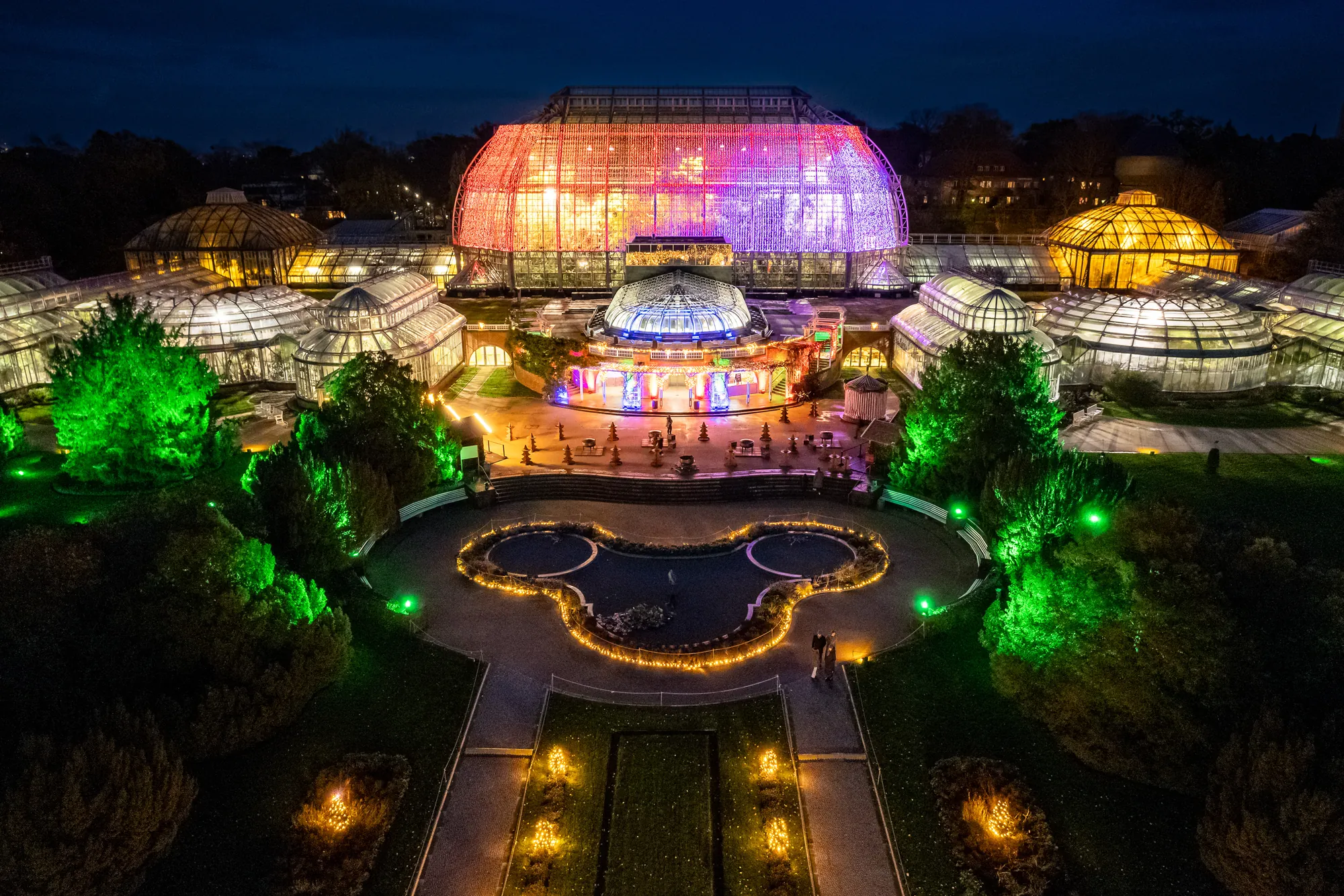 Christmas Garden 2023 - Aussicht auf das Tropenhaus bei Nacht, Gartenanlage und Gewächshäuser in gelben und bunten Farben