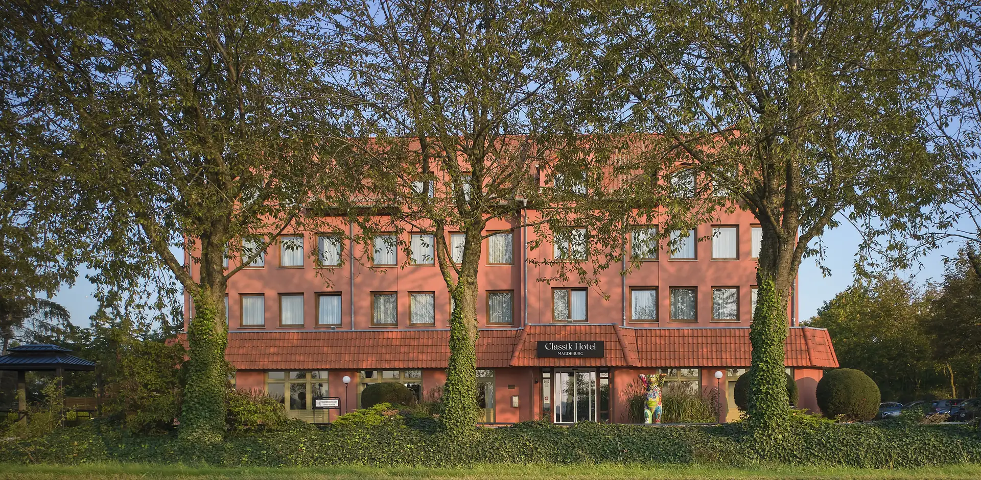 Mehrstöckiges Gebäude des Classik Hotel Magdeburg mit rechteckigen Fenstern und Bäumen im Vordergrund