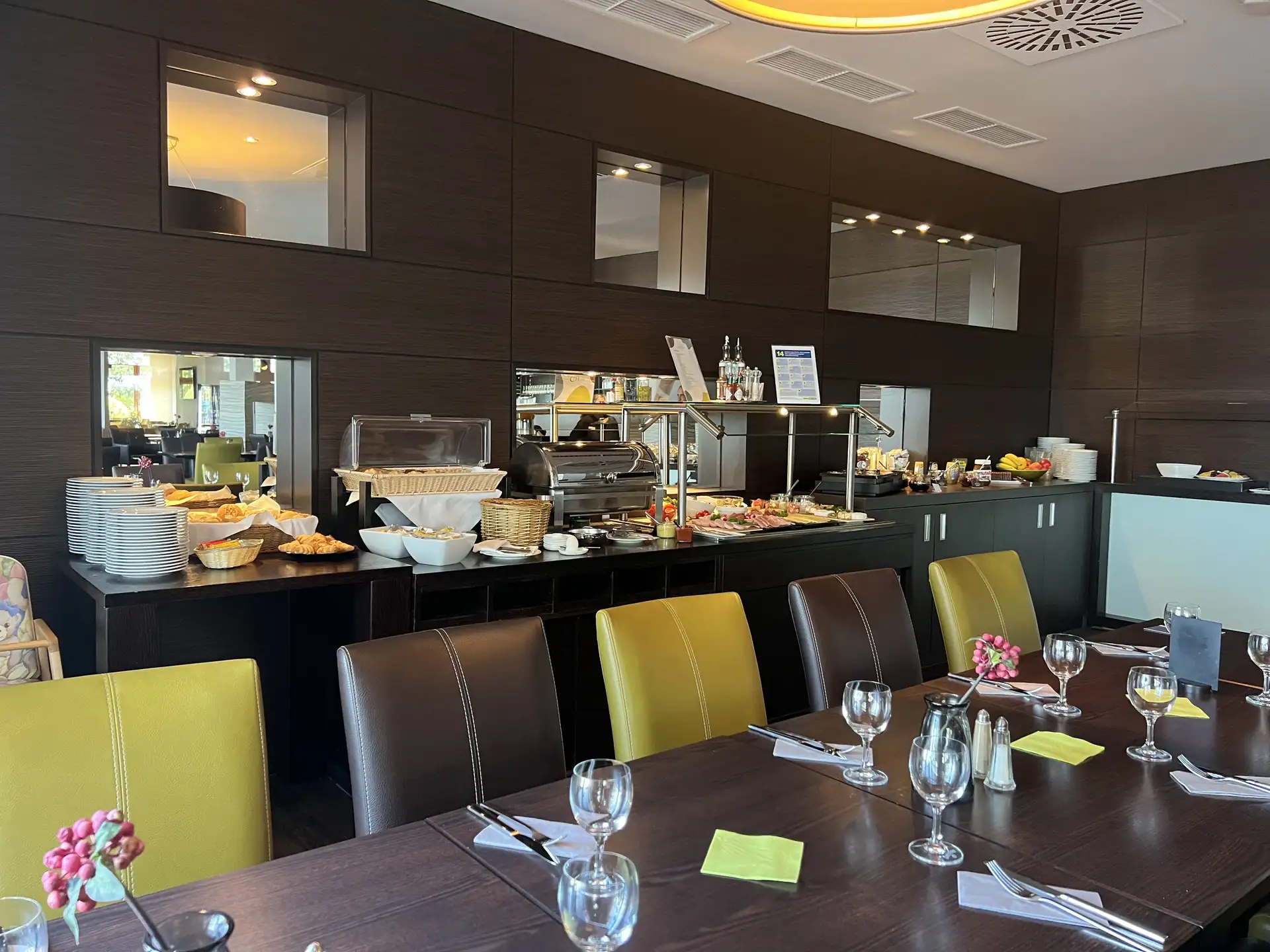 Buffet mit Frühstücksangebot und gedeckter Tisch mit Gläsern, Besteck und Servietten in einem modernen Hotelrestaurant