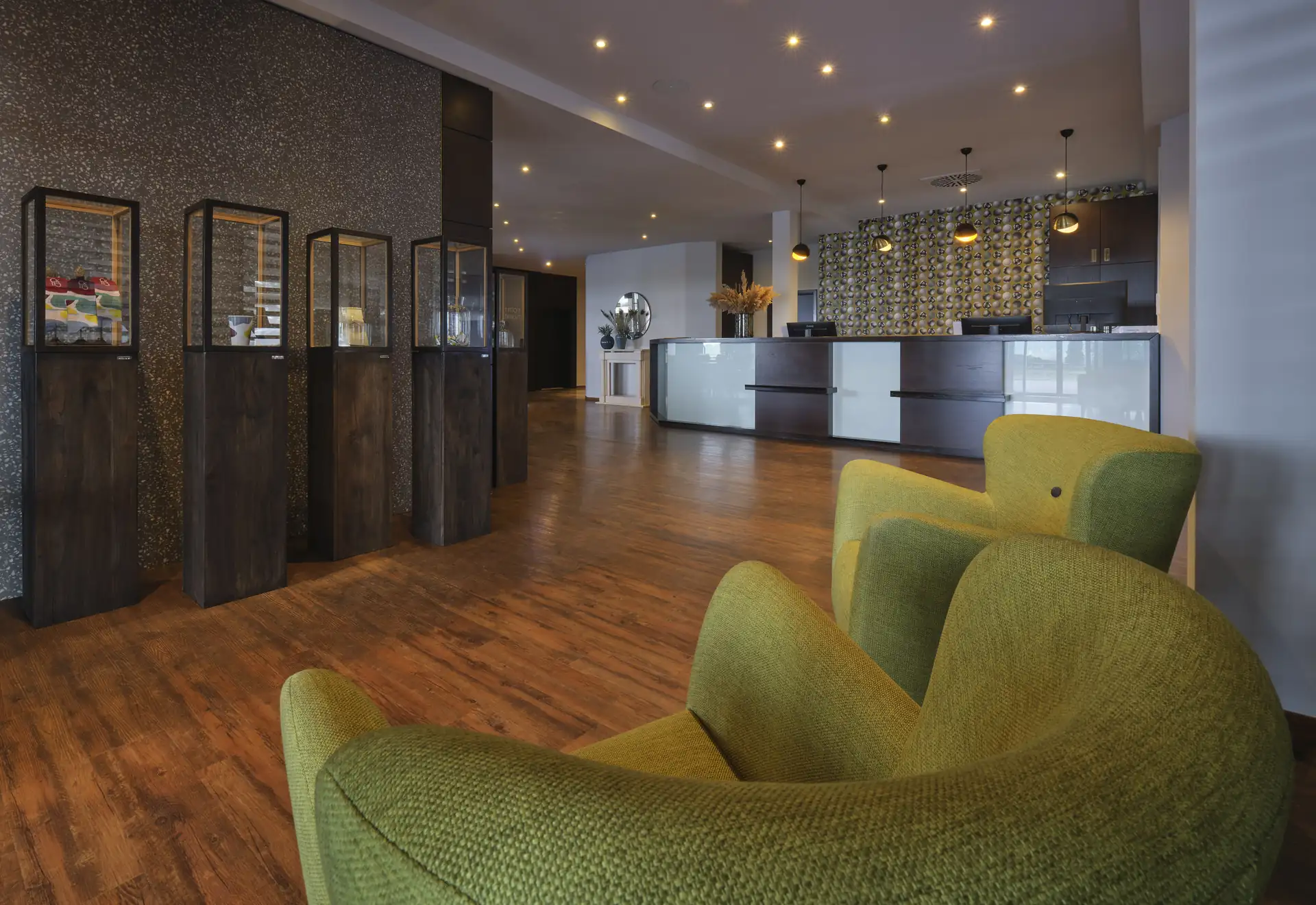 Lobby mit grünem Sessel im Vordergrund, dunklen Raumteilern mit Glas und einem Empfangstresen im Hintergrund im Classik Hotel Magdeburg