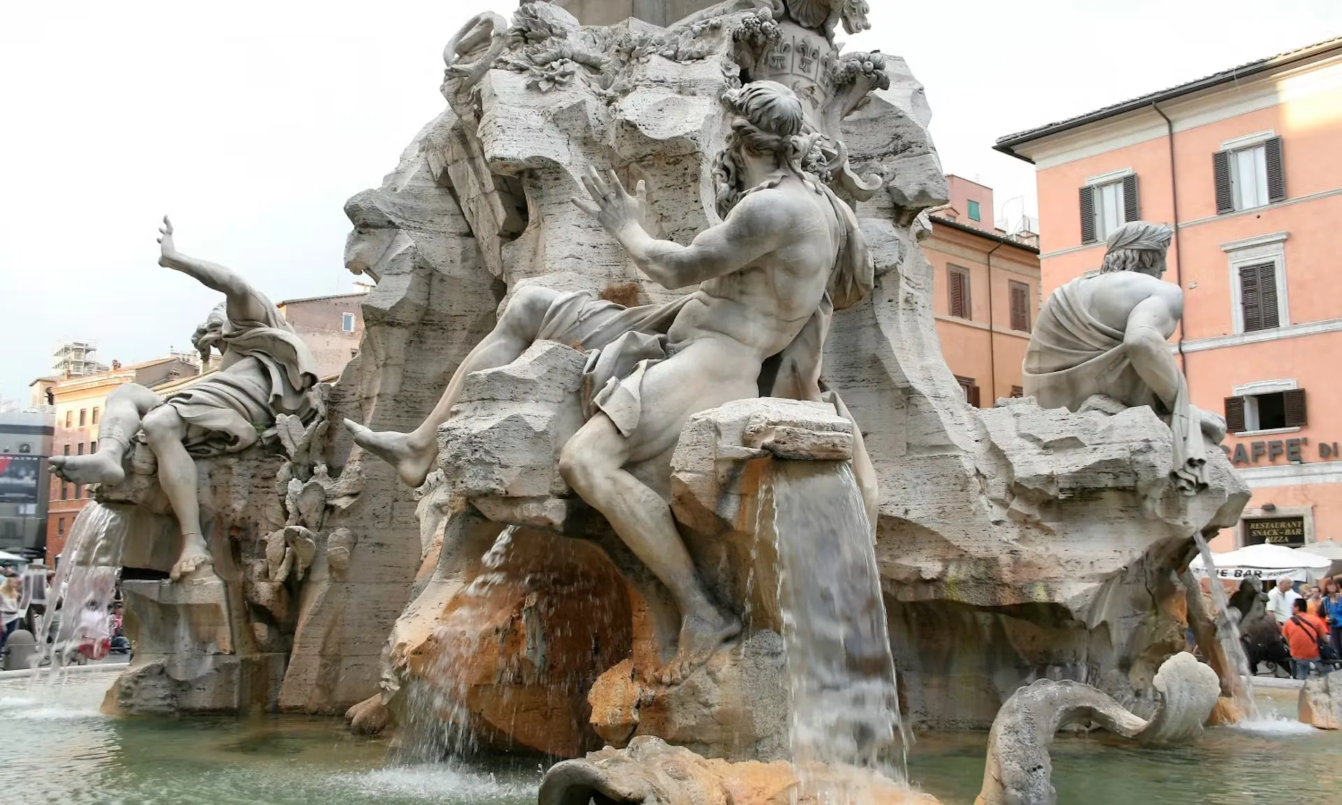 Das Bild zeigt eine Nahaufnahme des berühmten Vierströmebrunnens (Fontana dei Quattro Fiumi) auf der Piazza Navona in Rom, ein wichtiger Schauplatz auf der Dan Brown „Illuminati“-Tour. Der Brunnen, geschaffen von Gian Lorenzo Bernini, zeigt monumentale Figuren, die die vier großen Flüsse der Welt repräsentieren. Im Bild sind beeindruckende Details der Skulpturen zu sehen, die über Felsen und Wasserkaskaden thronen. Die kunstvolle Gestaltung und das fließende Wasser verleihen der Szene eine dynamische Atmosphäre, die den historischen und mystischen Charakter der Tour unterstreicht.