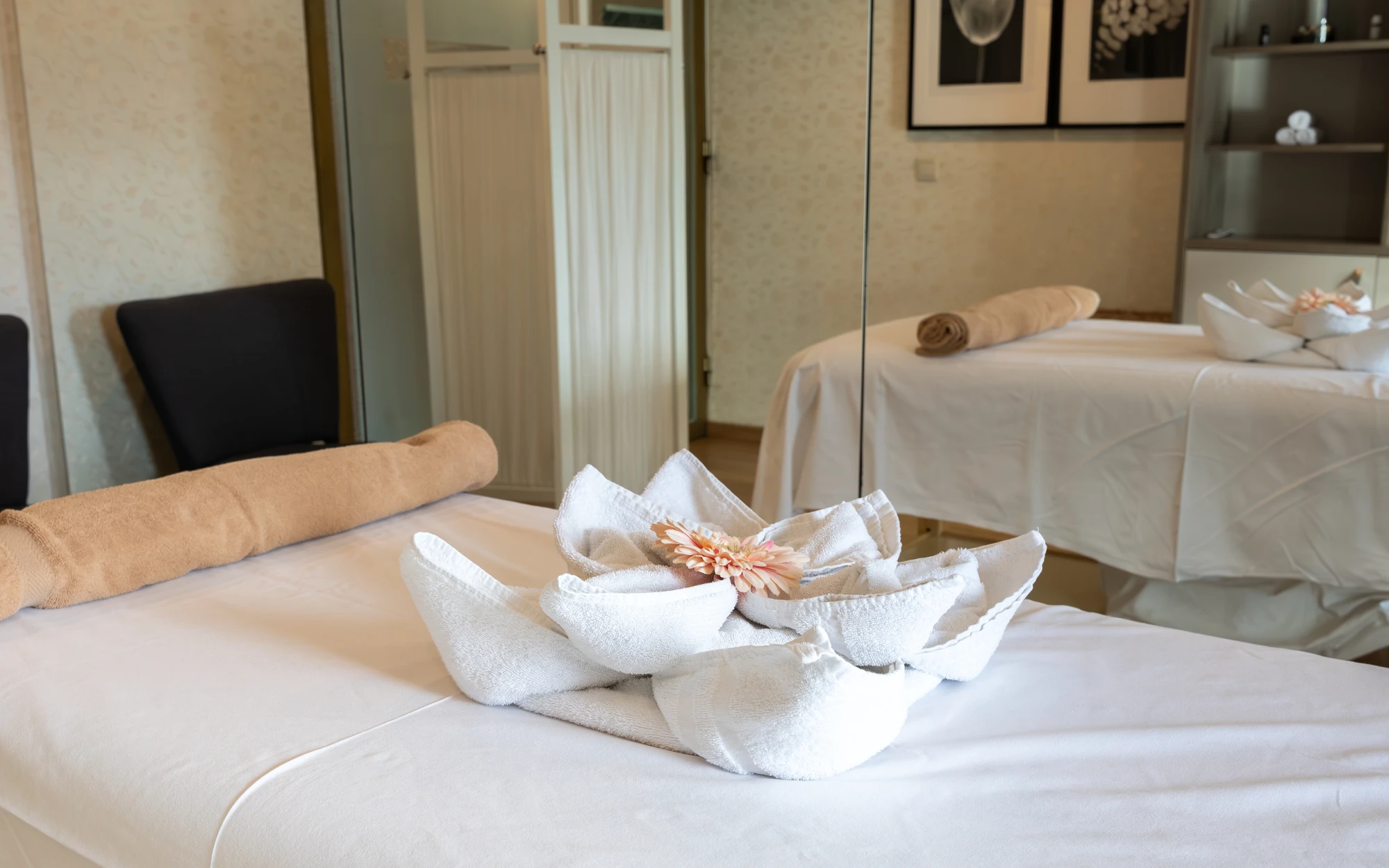 Blume aus weißen Handtüchern gefaltet und einer Blume darauf auf einer Massageliege vor einem Spiegel in einem Massageraum