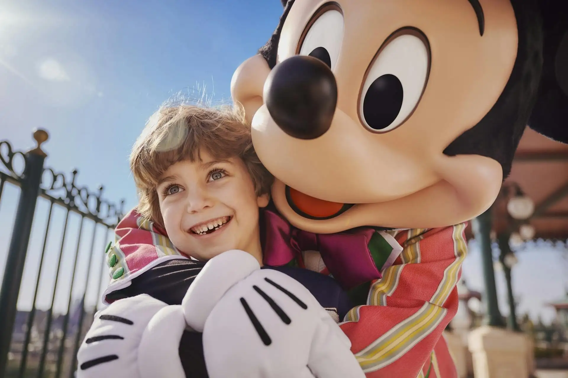 Mickey-Mouse-Figur umarmt ein Kind vor einem schmiedeeisernen Zaun im Freien