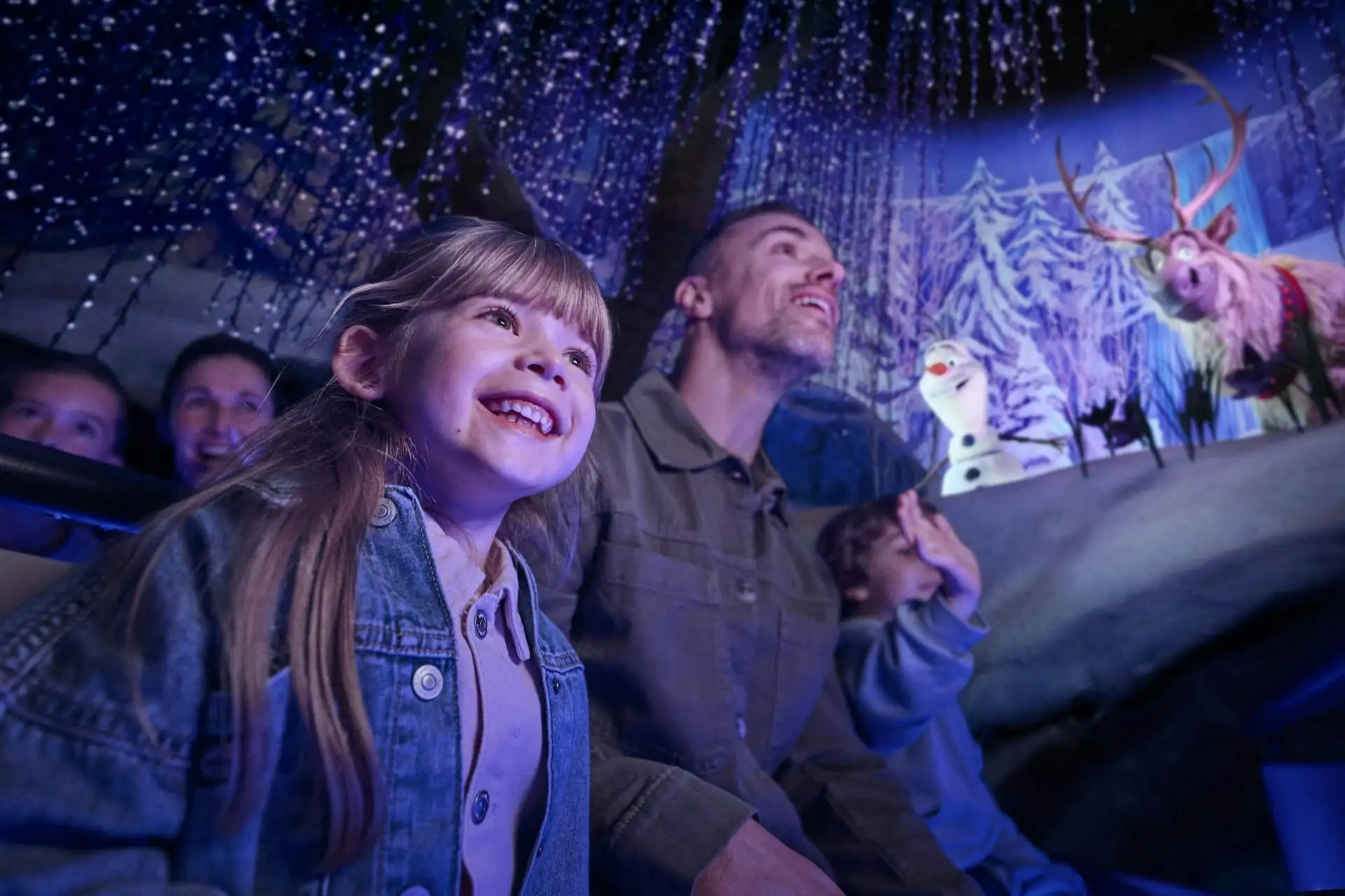 Familie mit zwei Kindern sitzt vor einer beleuchteten Kulisse mit Figuren aus dem Disney-Film 