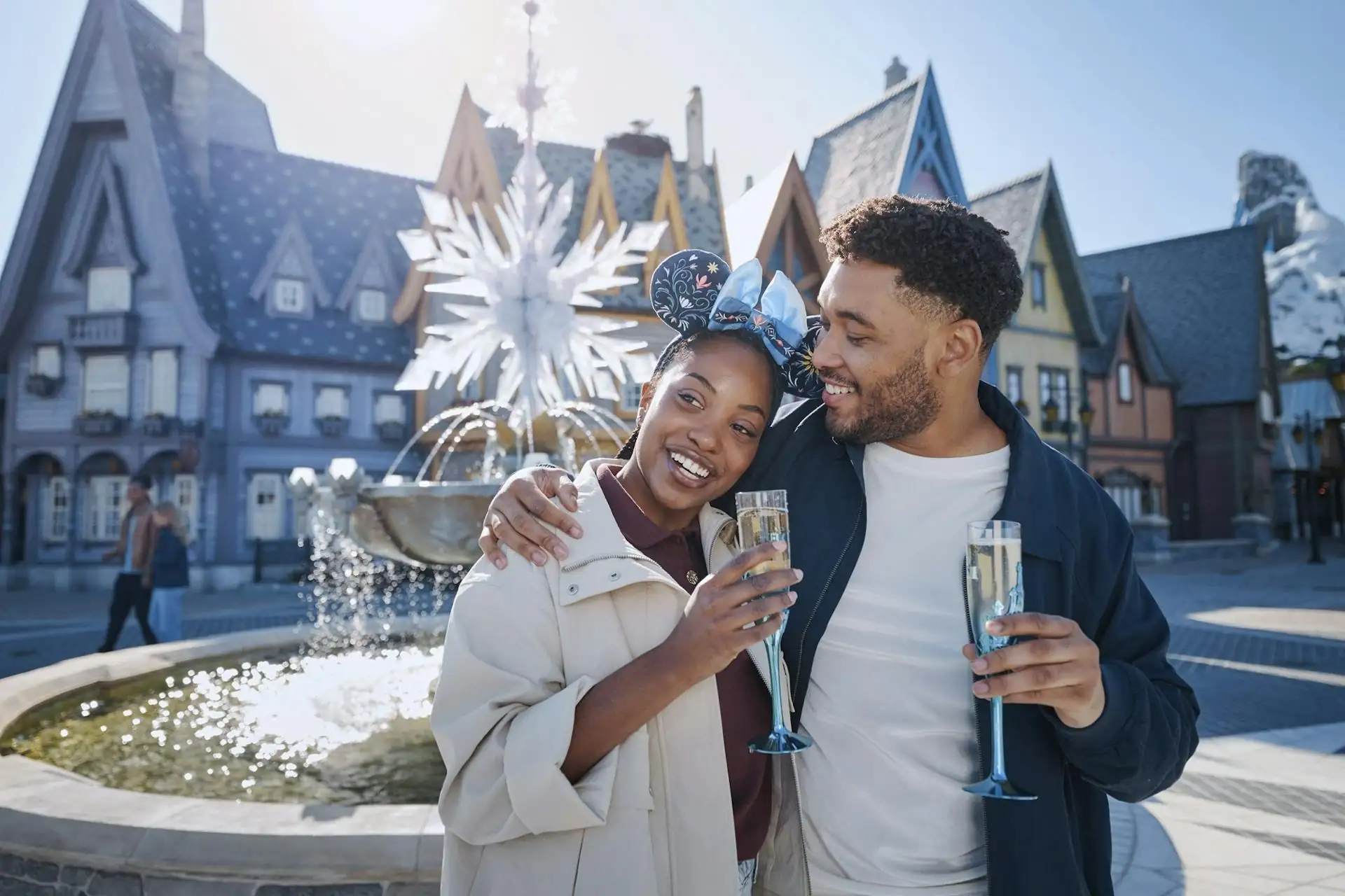 Paar mit Sektgläsern vor einem Brunnen und einem märchenhaften Gebäude im Disneyland Paris