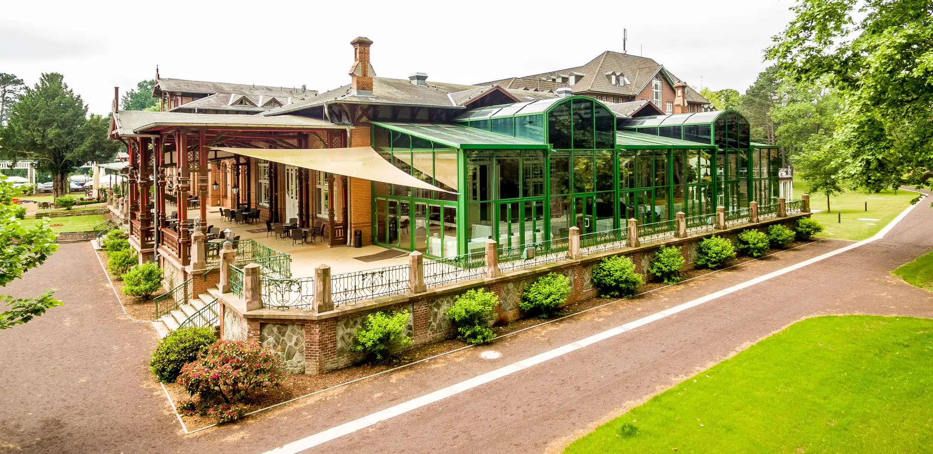 Luftaufnahme des Dorint Herrenkrug Parkhotels Magdeburg mit verglaster Terrasse und umlaufender Veranda in einem Park mit Wegen und Rasenflächen