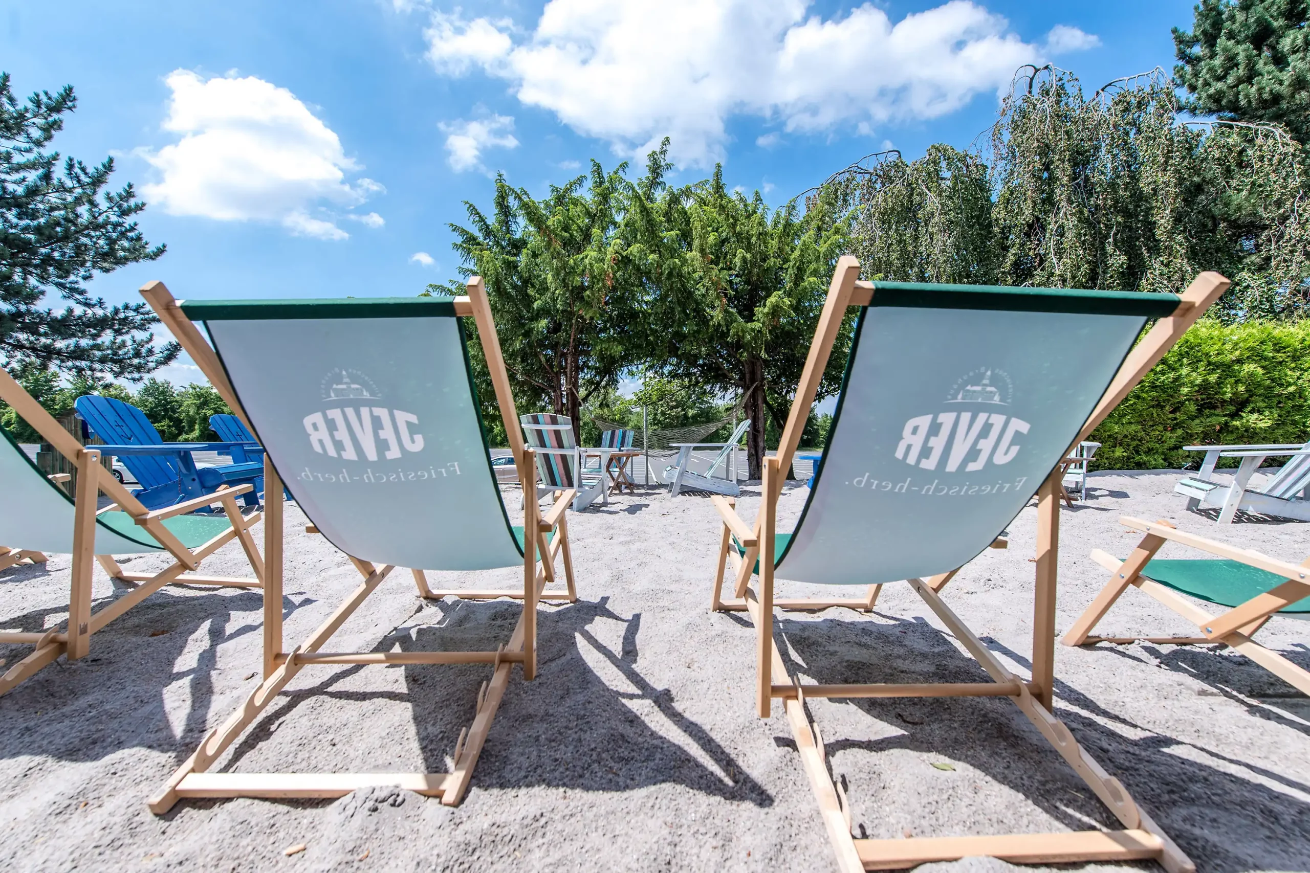 Zwei Strandkörbe mit hellgrünen Stoffen und weißem Aufdruck stehen auf Sand vor Bäumen und blauem Himmel im Dorint Hotel Alzey/Worms