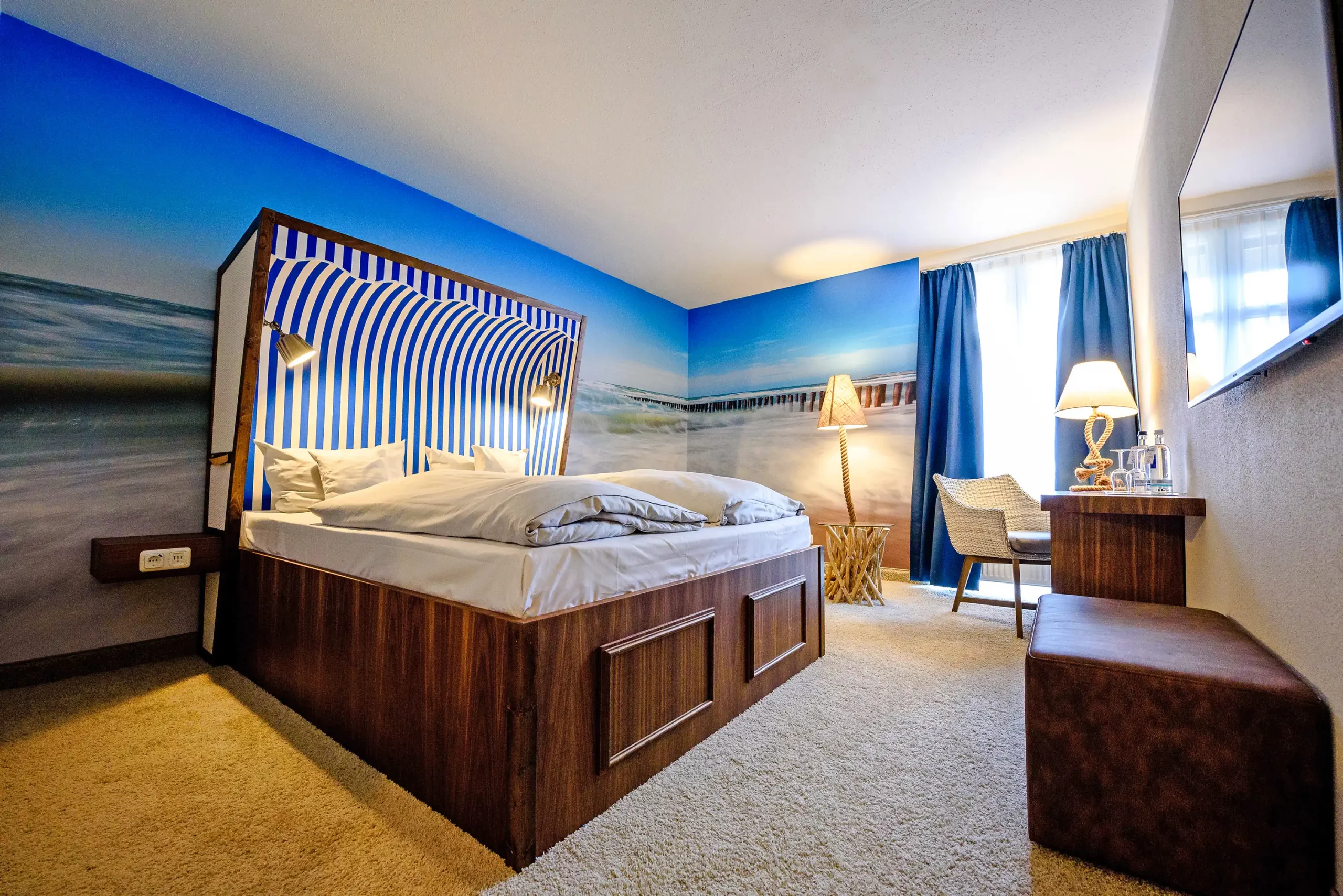 Standardzimmer mit Doppelbett, Wandbild mit Strandkorb und Meeresmotiv, Schreibtisch mit Stuhl, Stehlampe und großem Spiegel