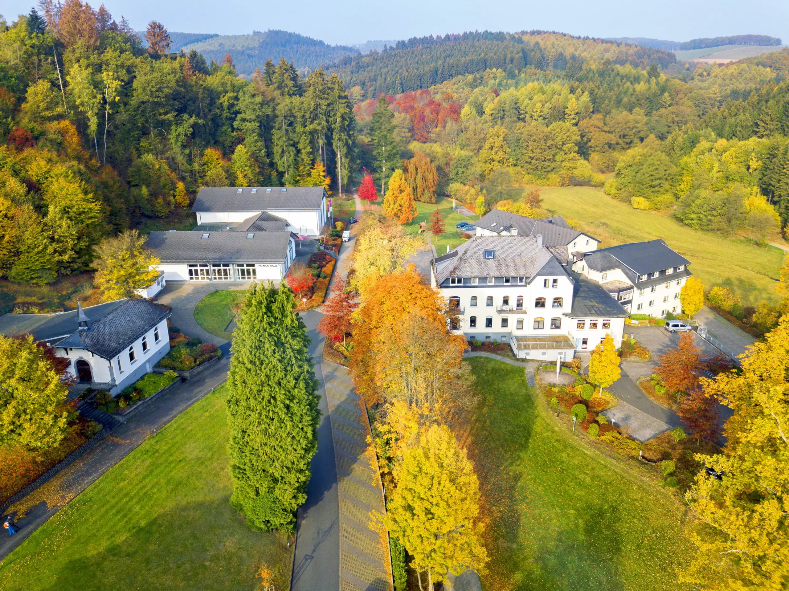 Luftaufnahme des Dorint Parkhotel Siegen mit mehreren Gebäuden, herbstlich gefärbten Bäumen und umliegender Waldlandschaft