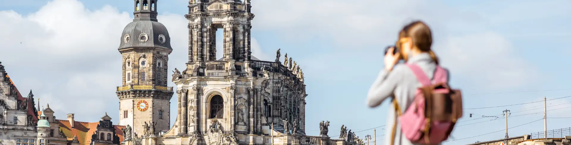 Blick auf die Türme der Dresdner Frauenkirche im Hintergrund und eine Person mit Rucksack, die mit einer Kamera fotografiert