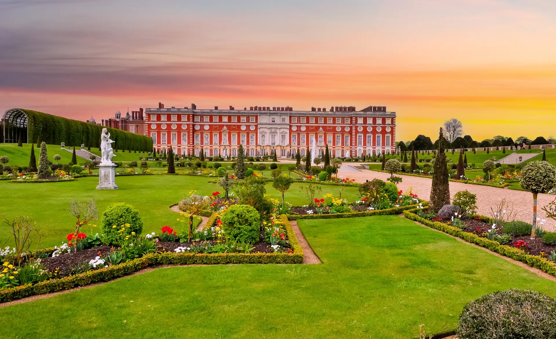 Hampton Court Palace Garden: wunderschön angelegte Gärten mit Herrenhaus im Hintergrund bei traumhaften Sonnenuntergang.