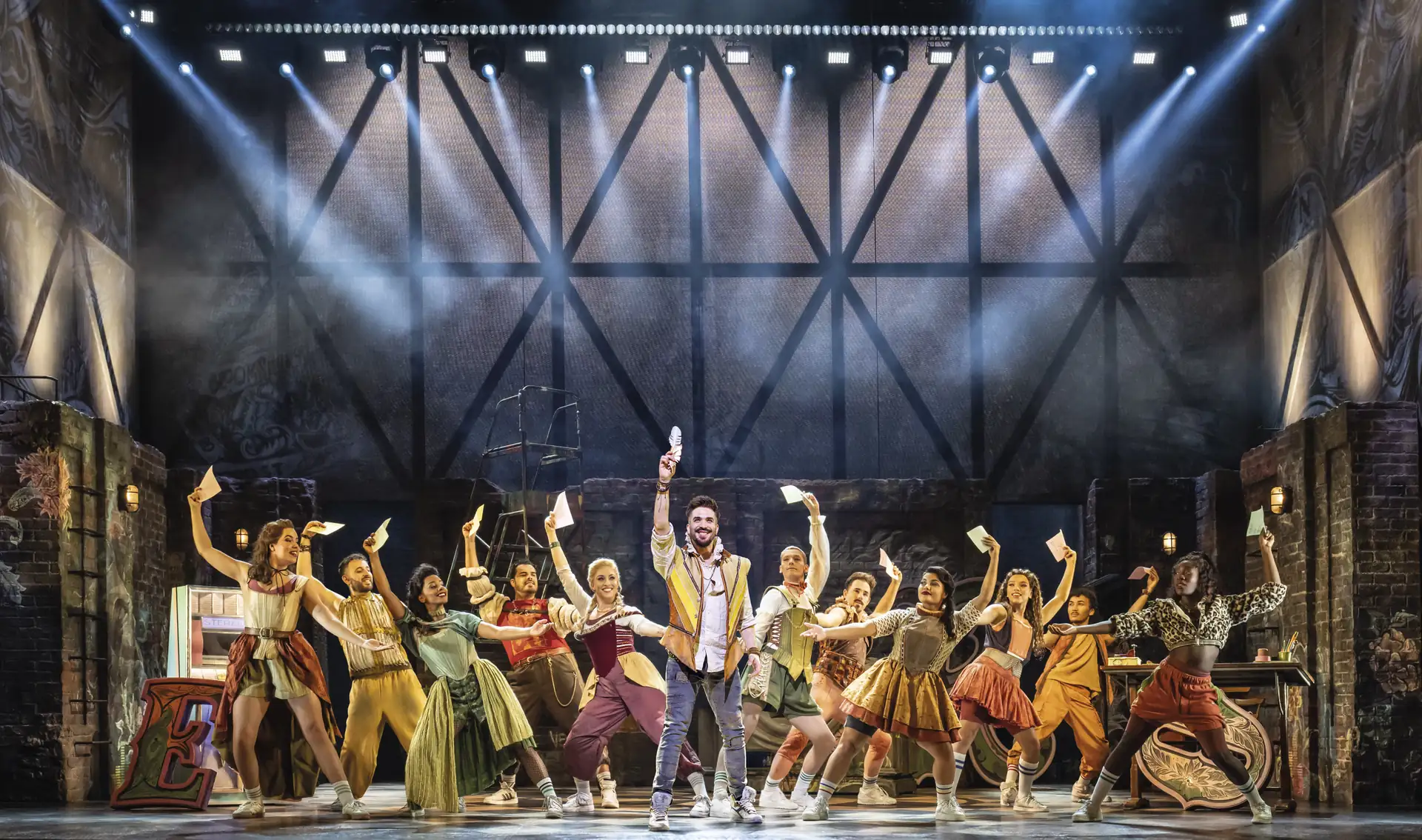 Ensemble des Musicals »& Julia – Das Pop Musical« auf der Bühne in dynamischer Pose mit erhobenen Armen und Mikrofon unter Bühnenbeleuchtung und Nebeleffekten