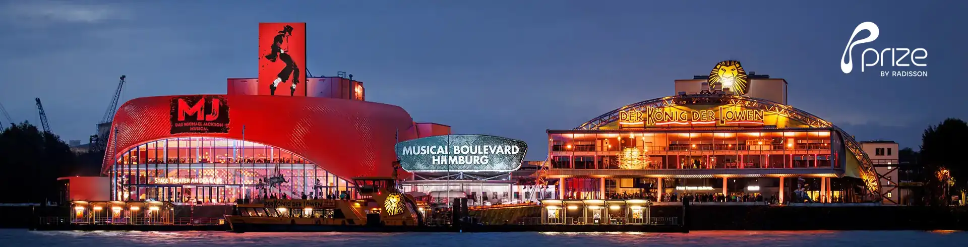 Panoramaaufnahme des Musical Boulevard Hamburg mit beleuchteten Gebäuden und dem Schriftzug 'Musical Boulevard Hamburg' bei Dämmerung