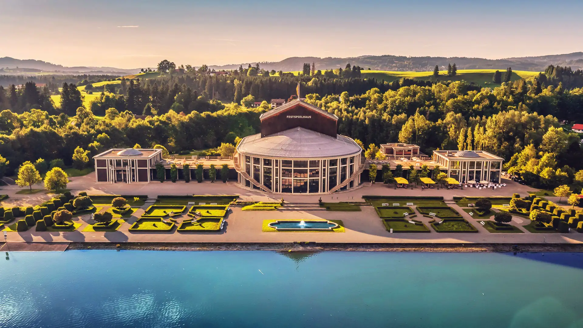 Festspielhaus Neuschwanstein, Außenaufnahme bei Sonnenschein mit Forggensee im Vordergrund