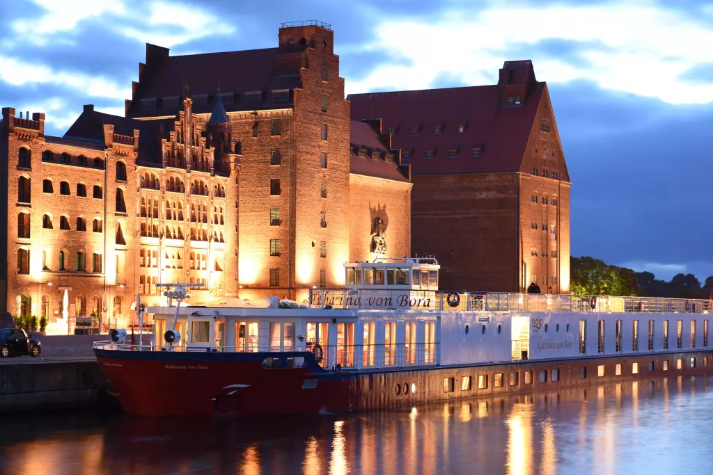 Beleuchtetes historisches Backsteingebäude am Wasser mit angelegtem Passagierschiff