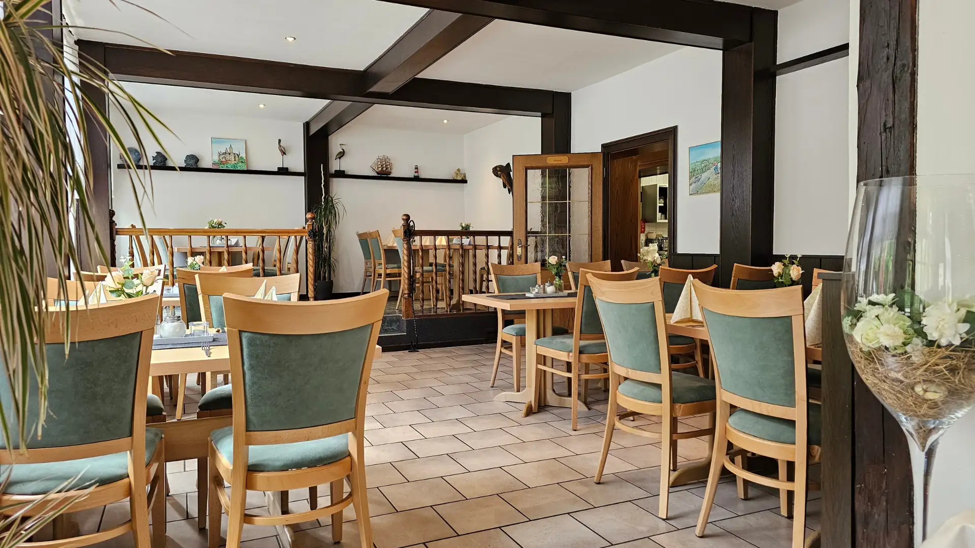 Gastraum des Restaurants im Ferienhotel Forelle mit Holztischen und Stühlen mit grünen Polstern, gedeckt mit weißen Servietten und Blumen.