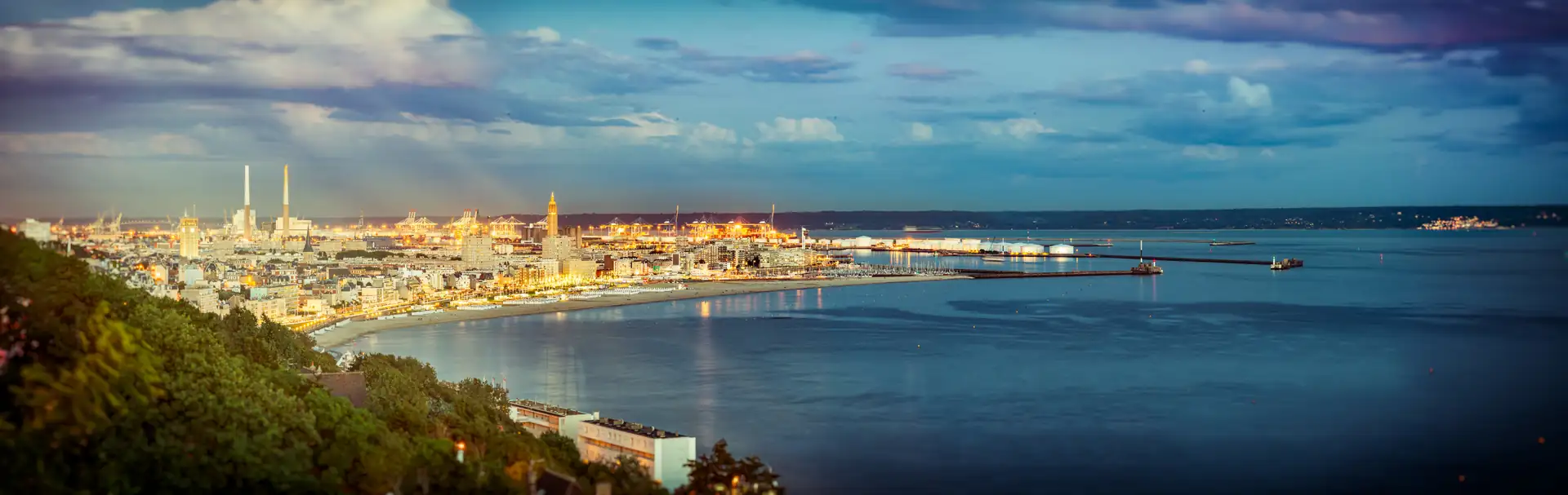 Panoramablick auf die Hafenstadt Le Havre mit Industrieanlagen, Hafenanlagen und ruhiger See unter bewölktem Himmel.