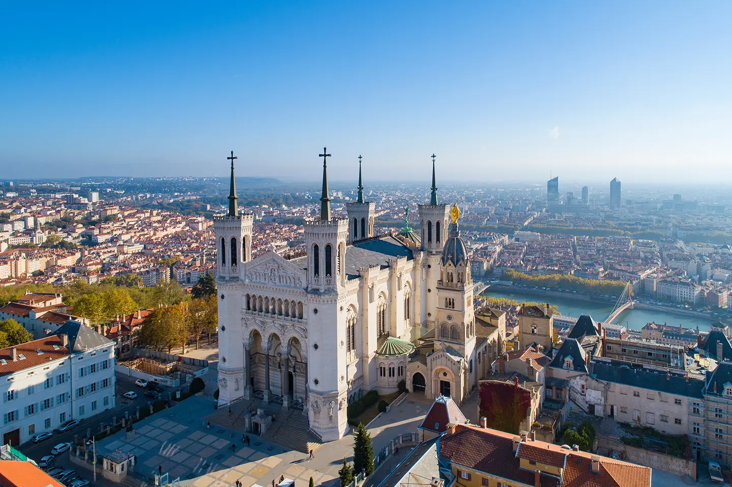 Luftbild von Lyon im Vordergrund, mit der Basilika von Notre Dame de Fourvière und der Stadtlandschaft bei Tageslicht, die die architektonische Vielfalt und Schönheit der Region zeigt.