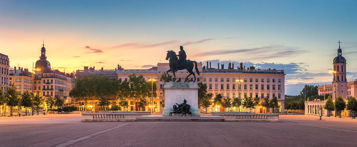 Place de Bellecour in Lyon im Abendlicht mit dem Reiterstandbild von Ludwig XIV bei Sonnenuntergang. Die Stadtbeleuchtung schafft eine warme, angenehme Atmosphäre.