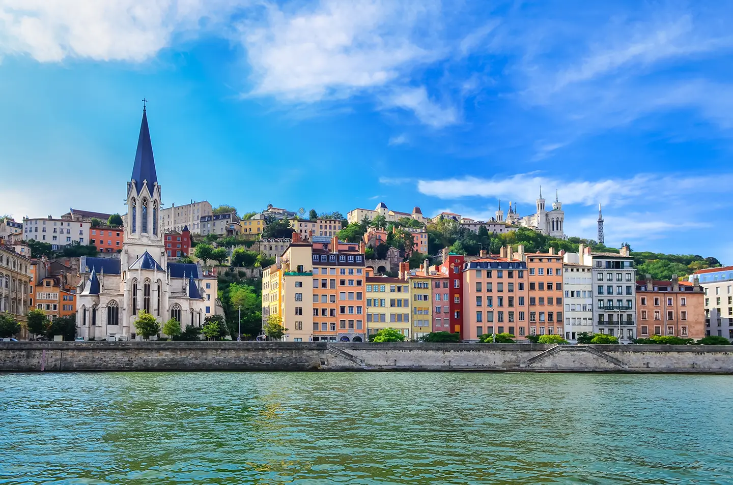 Blick auf die bunten Häuser von Lyon vom Wasser aus, bei sonnigem Wetter, das die lebhafte Atmosphäre der Stadt unterstreicht.