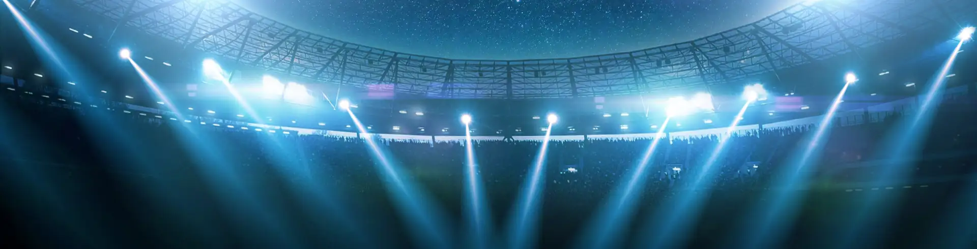 Blick in ein großes Stadion mit hellen Scheinwerfern, die von der Tribüne auf das Spielfeld strahlen.