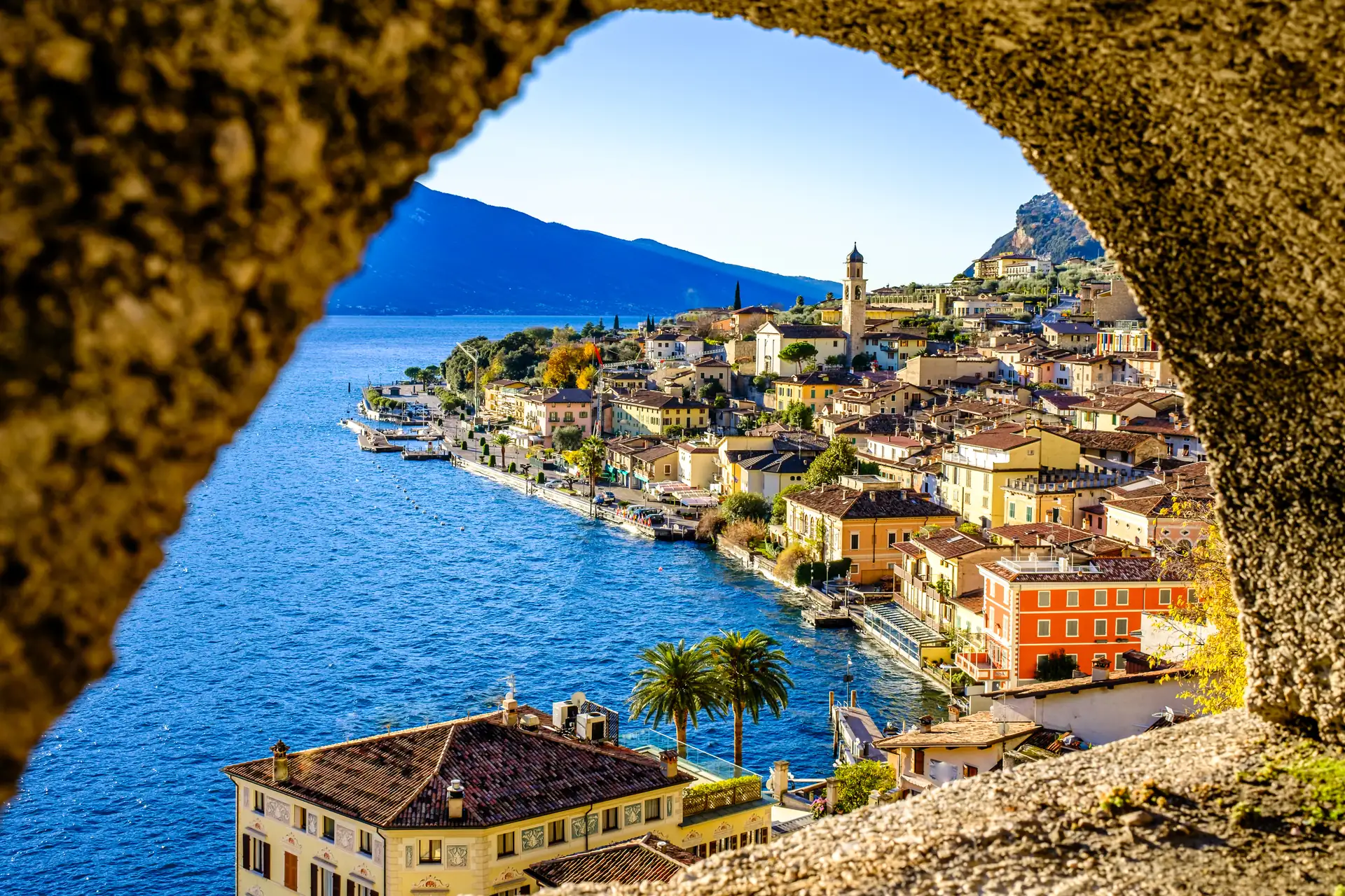 Blick durch einen Felsenbogen auf die Uferpromenade und den Ort Limone sul Garda am Gardasee mit Bergen im Hintergrund