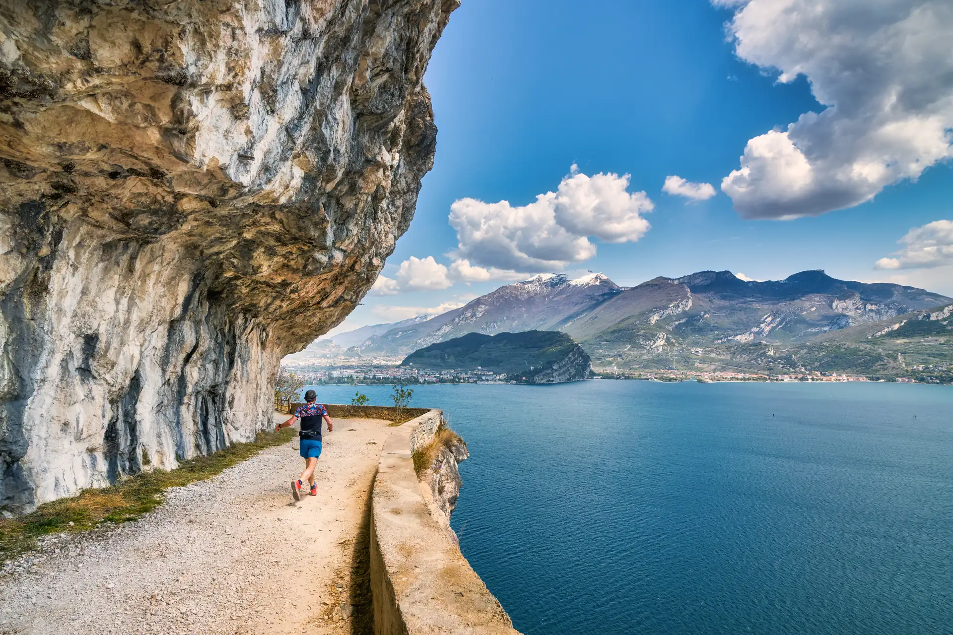 Läufer auf schmalem Wanderweg an Felswand (Strada del Ponale) mit Blick auf den Gardasee und Berge bei Riva del Garda