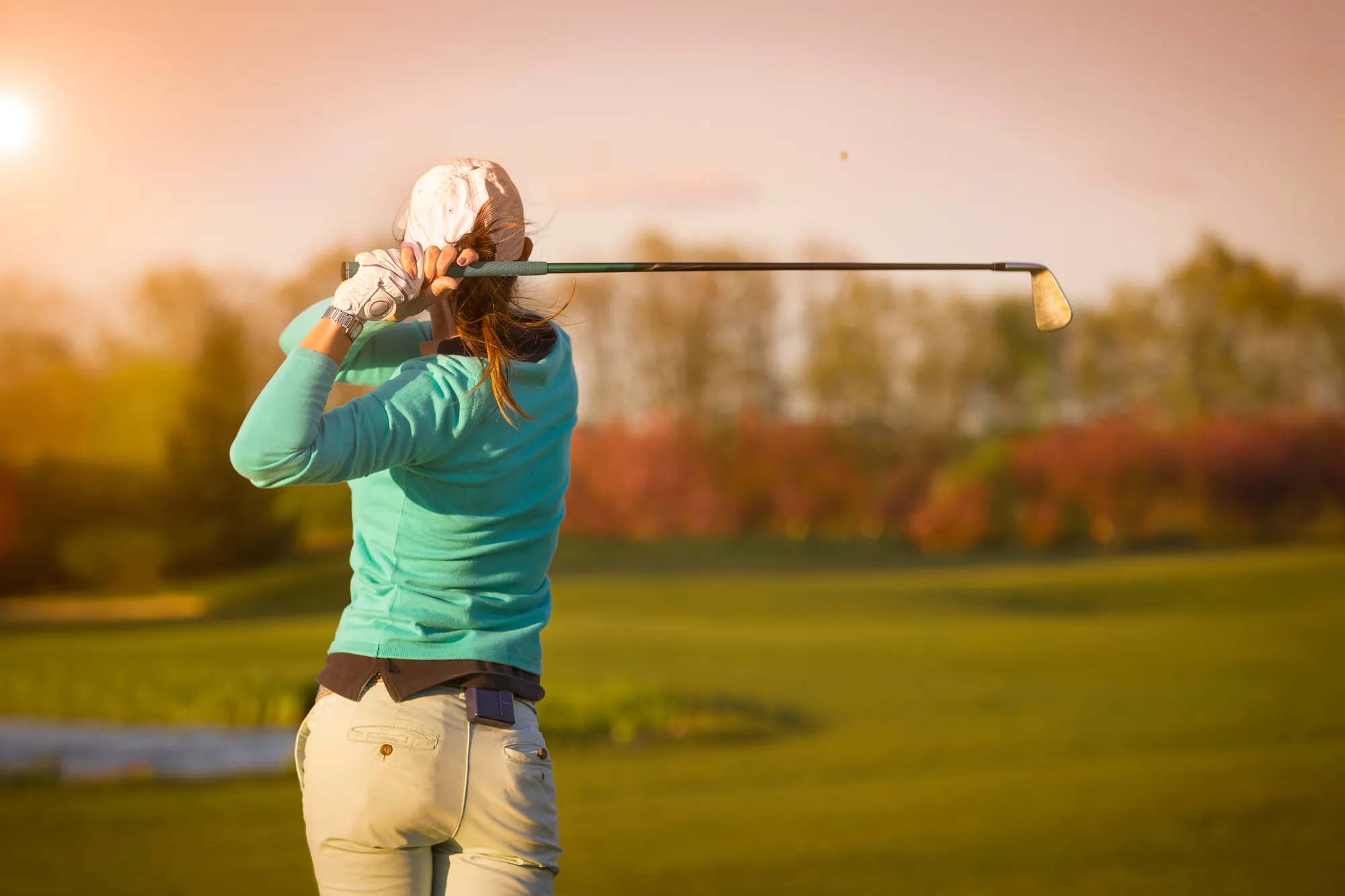 Golf - Frau mit Golfschläger hat den Golfball getroffen und schaut seiner Flugkurve nach.