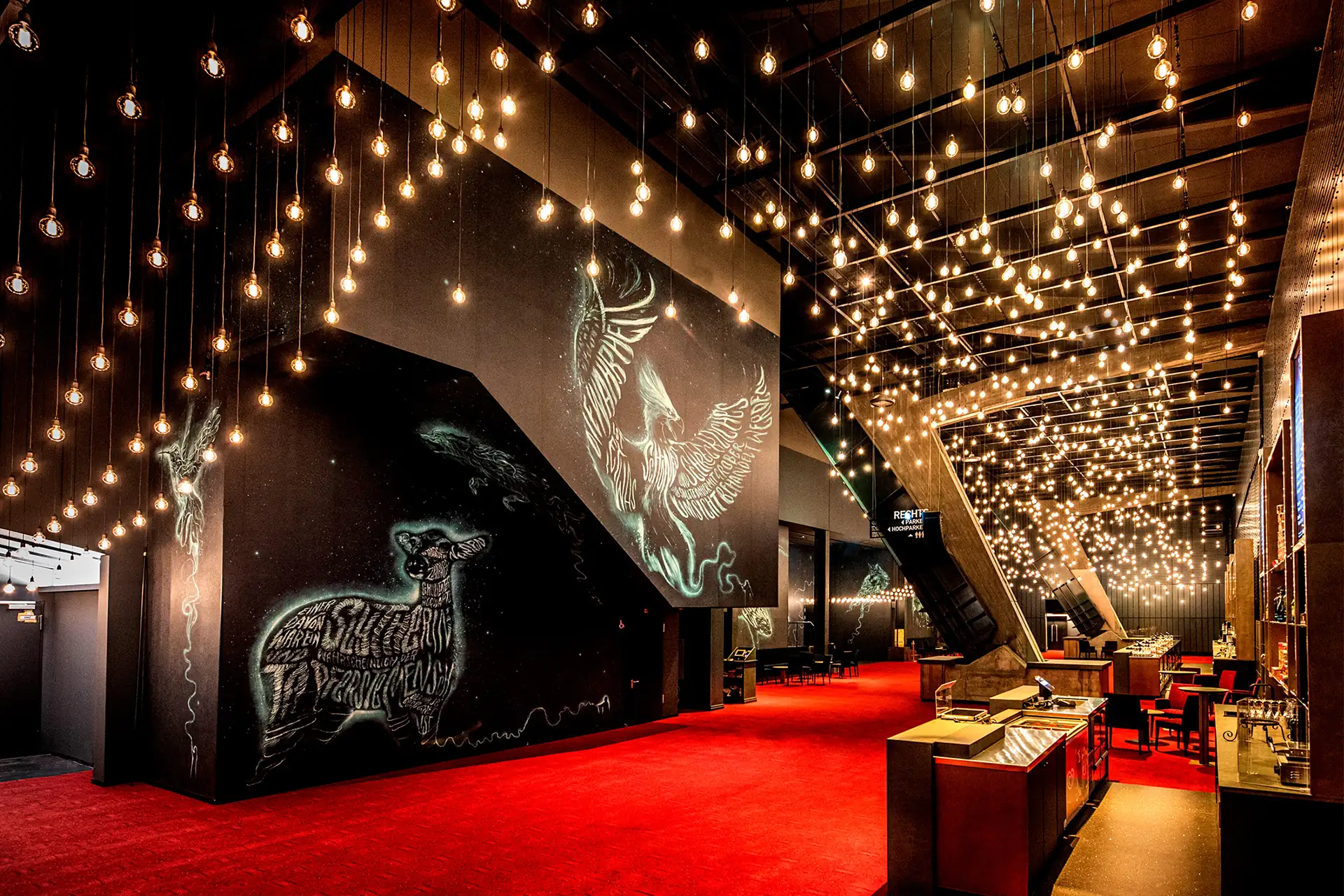 Harry Potter und das verwunschene Kind in Hamburg: Foyer mit zahlreichen hängenden Deckenlampen, Patronussen an den Wänden und Barbereich.