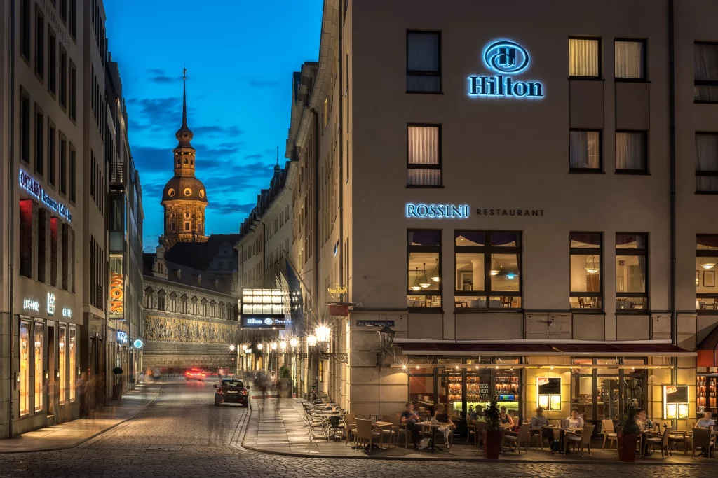 Außenansicht Hilton Dresden mit Außenplätzen vom Rossini Restaurant am Abend - im Hintergrund die Heiliggeistkirche