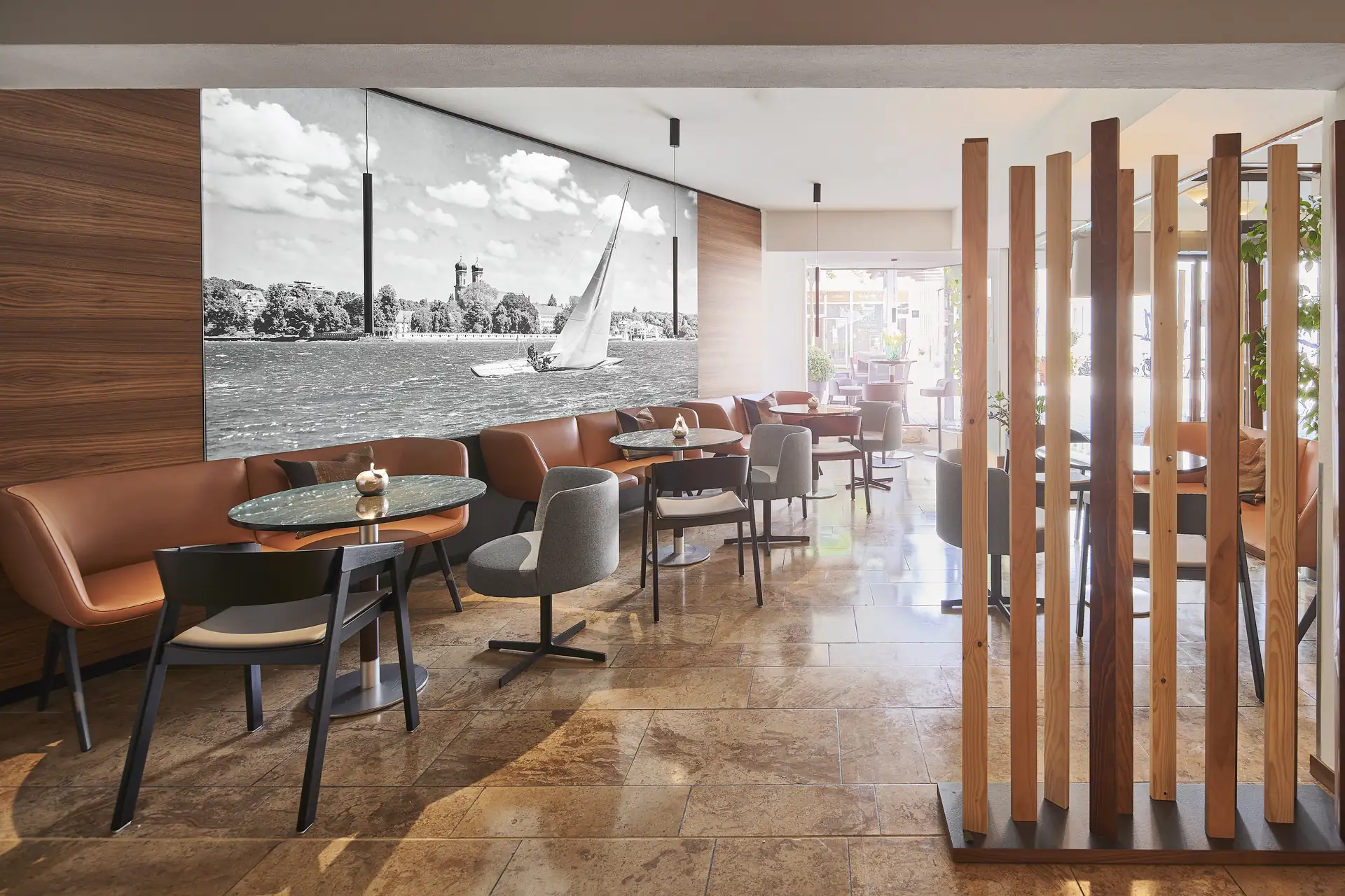 Hotel City Krone: Innenansicht des Restaurants mit braunen und grauen Sitzmöbeln, runden Tischen und einer großen Schwarz-Weiß-Wandgrafik eines Segelbootes auf Wasser.