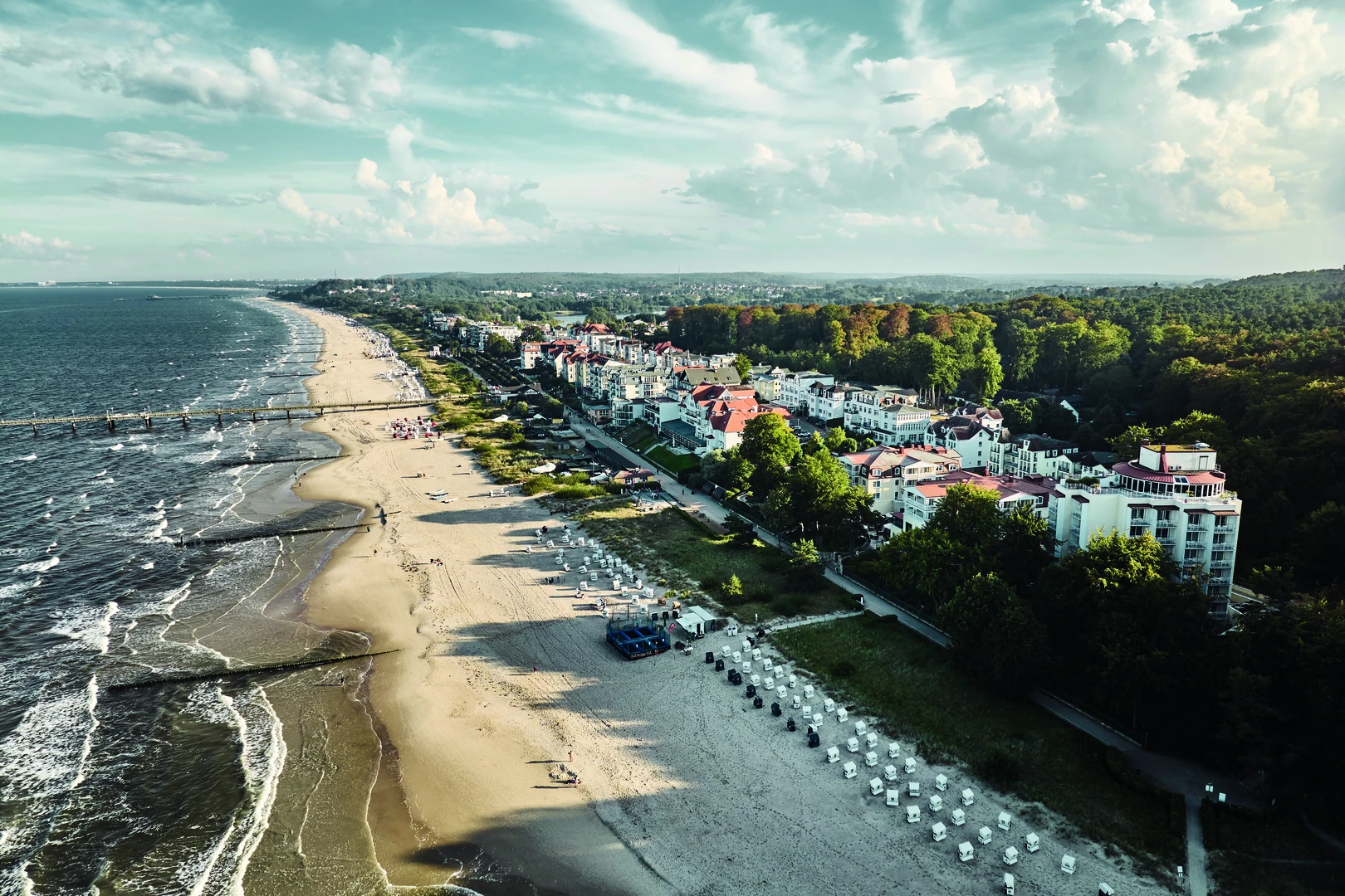 Ein malerischer Blick auf die Küste von Bansin mit dem aja Strandhotel Bansin im Vordergrund: Die beeindruckende Kombination aus Sandstrand, Ostsee und charmanten Villen schafft eine einladende Urlaubsatmosphäre. Das weitläufige Ufer und die lebendige Promenade bieten die perfekte Kulisse für erholsame Spaziergänge und unvergessliche Tage am Meer.