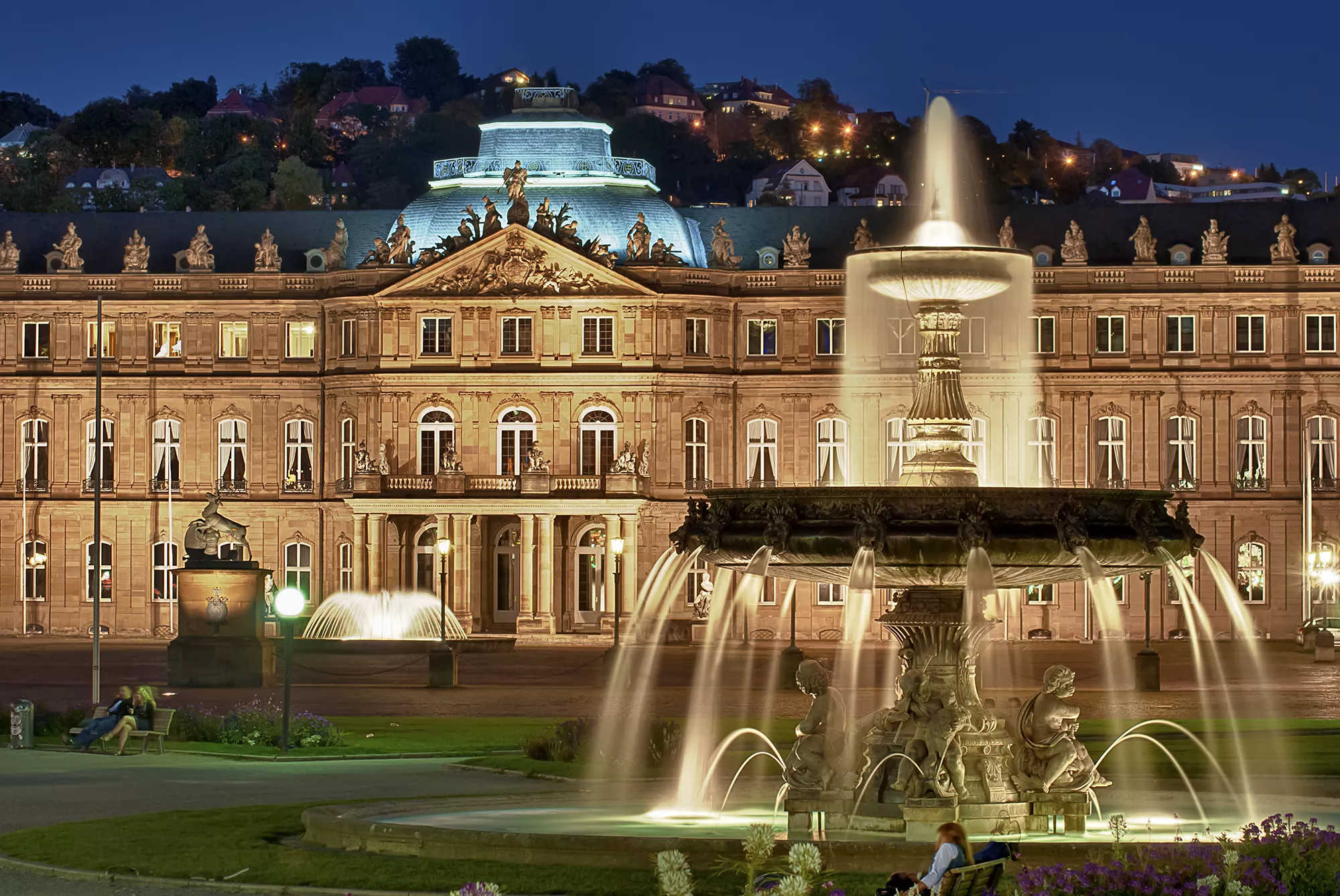 Das beleuchtete Neue Schloß mit Schloßplatz und Springbrunnen bei Nacht, bei einem Besuch mit Hotel in Stuttgart