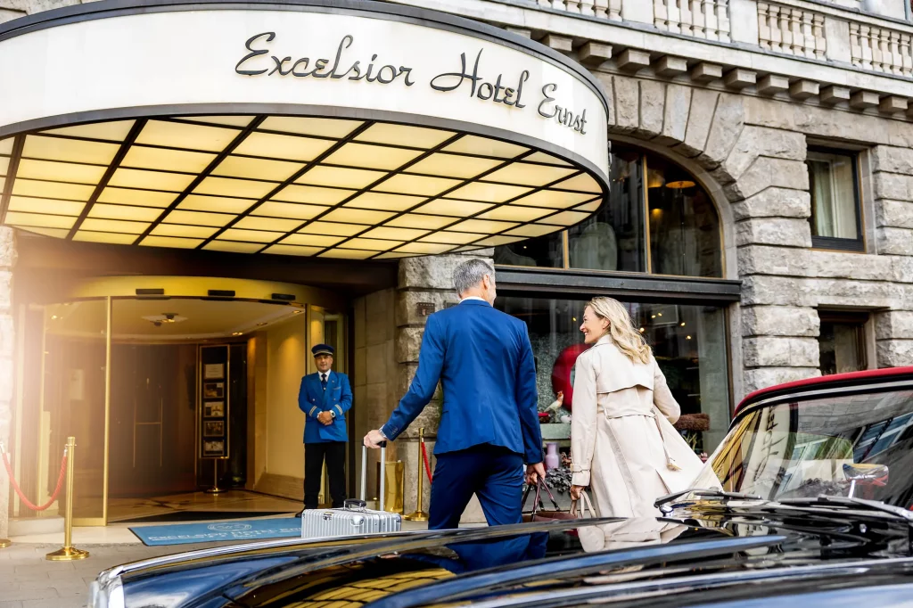 Paar tritt in das Luxus Hotel Excelsior Hotel Ernst, eines der Hotels in Europa, ein - Doorman erwartet die Gäste