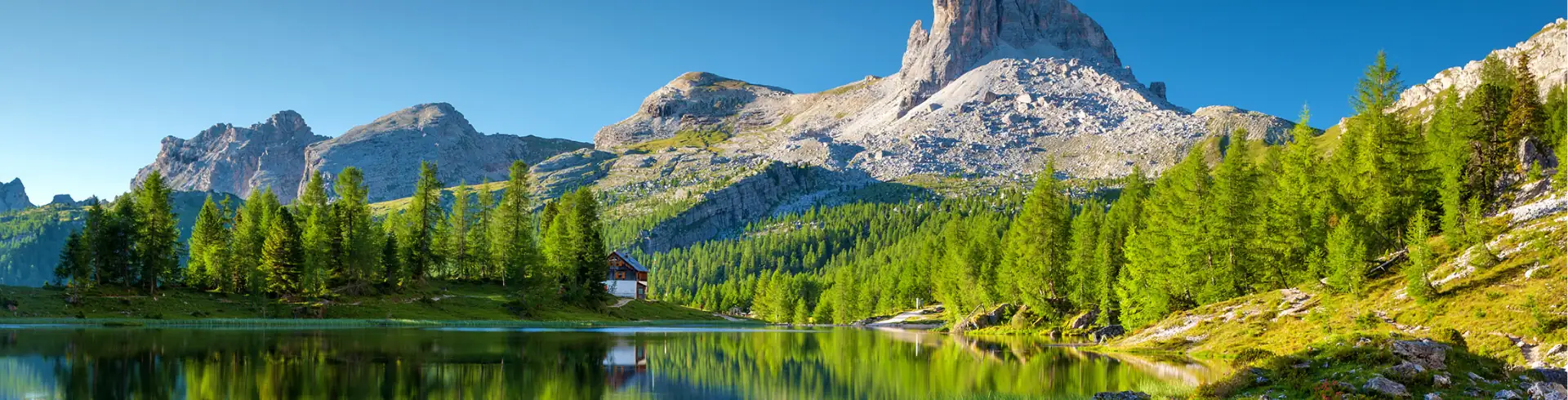 In die Natur Symbolbild im Bannerformat: Malerische Landschaft mit Berg und einzelnem Haus am See.