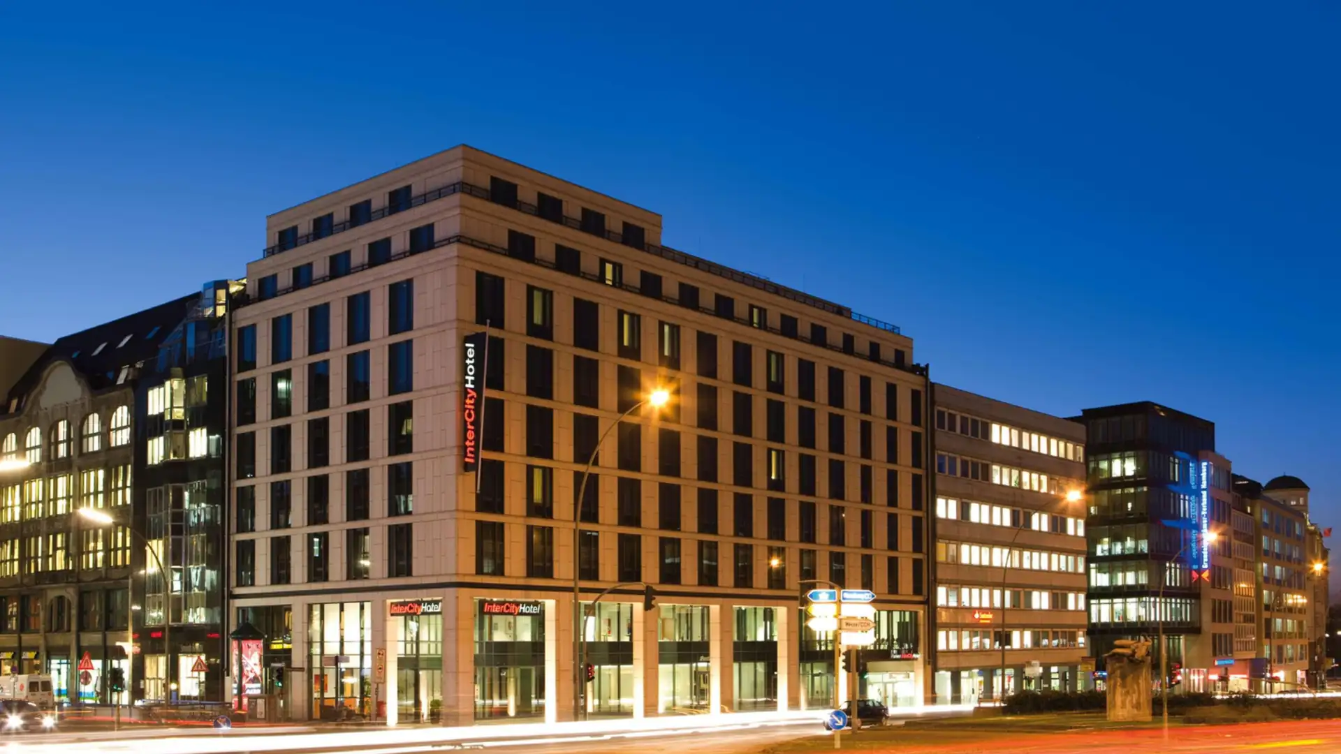 IntercityHotels im Kachelformat: IntercityHotel in einem mehrstöckigen Gebäude bei Abenddämmerung, beleuchtete Fenster und Straßenlaternen