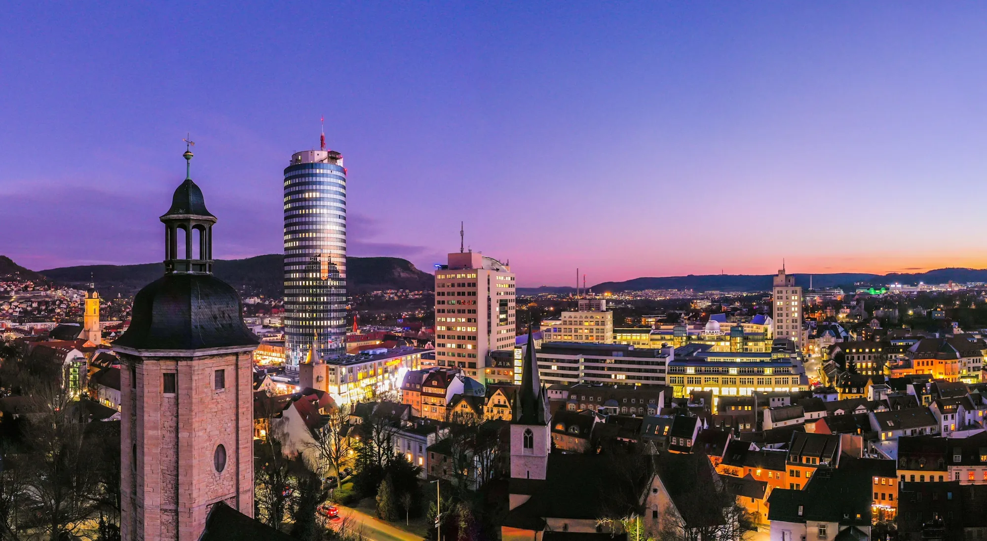 Grandioses Panoramabild mit Sonnenuntergang über Lichterstadt Jena und Blick auf den erleuchteten JenTower.